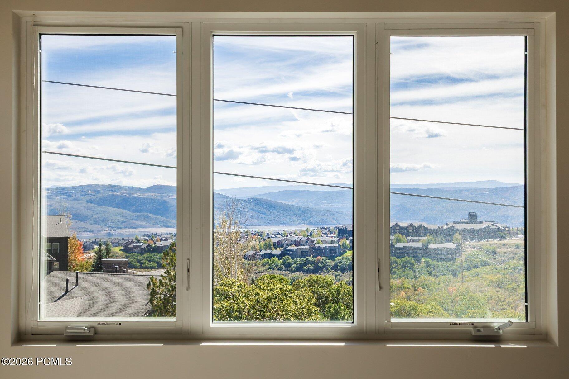 Mountain valley and neighborhood viewed through three large windows, with a distant lake and autumn foliage.