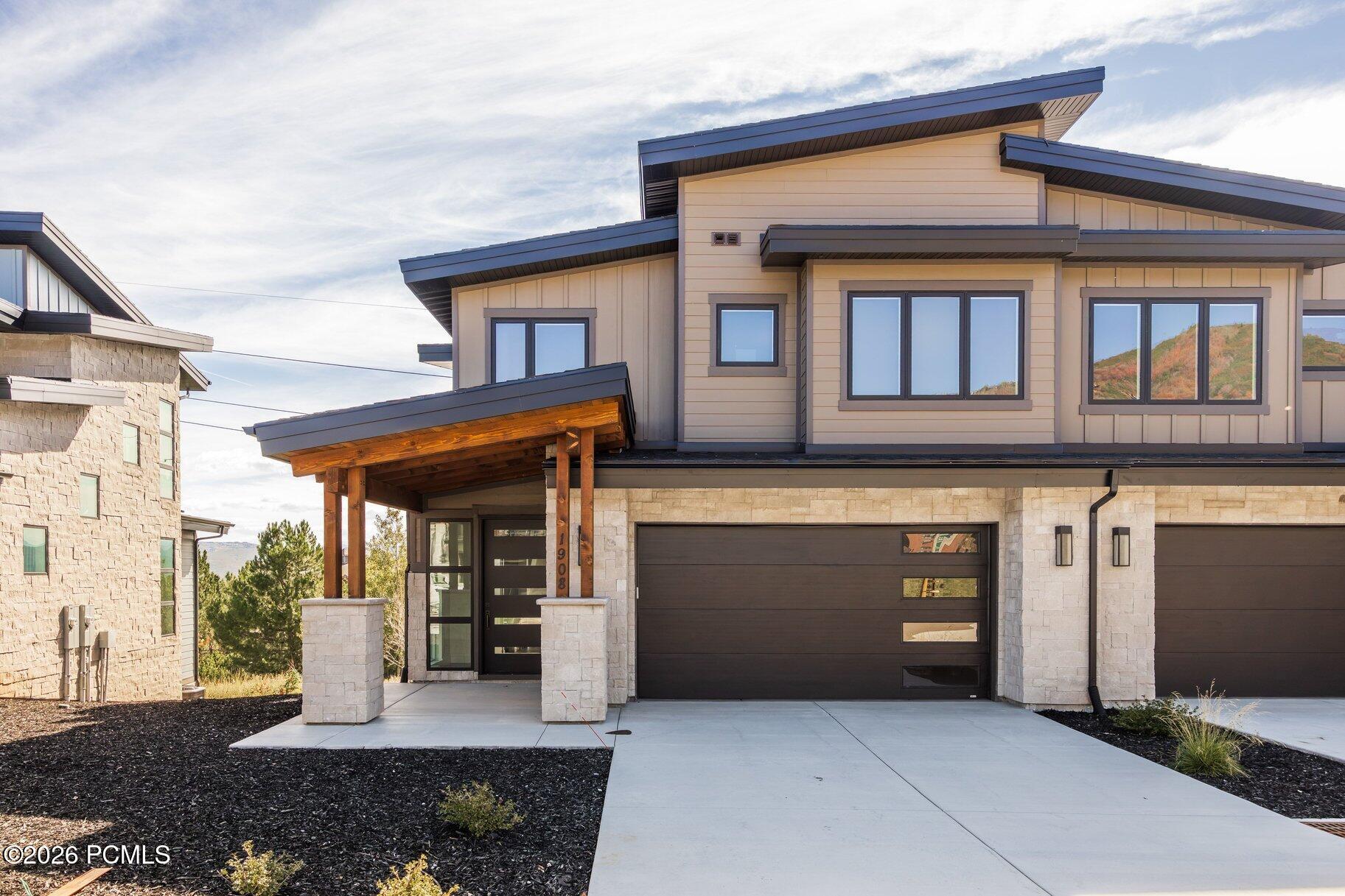 Modern two-story home with stone veneer, angular rooflines, covered wood entry, and wide driveway.