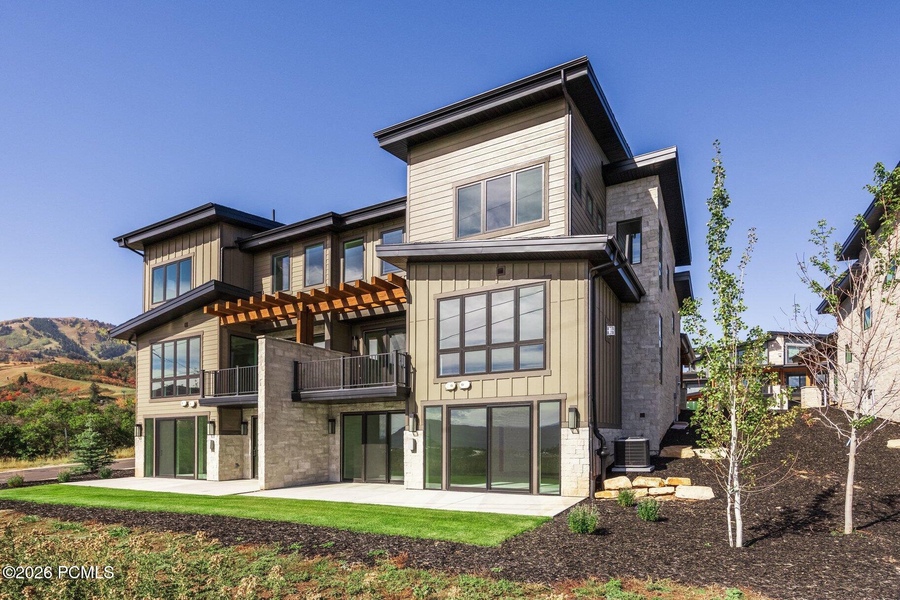 Modern multi-story home with stone accents, a wood pergola, and hills in the background.