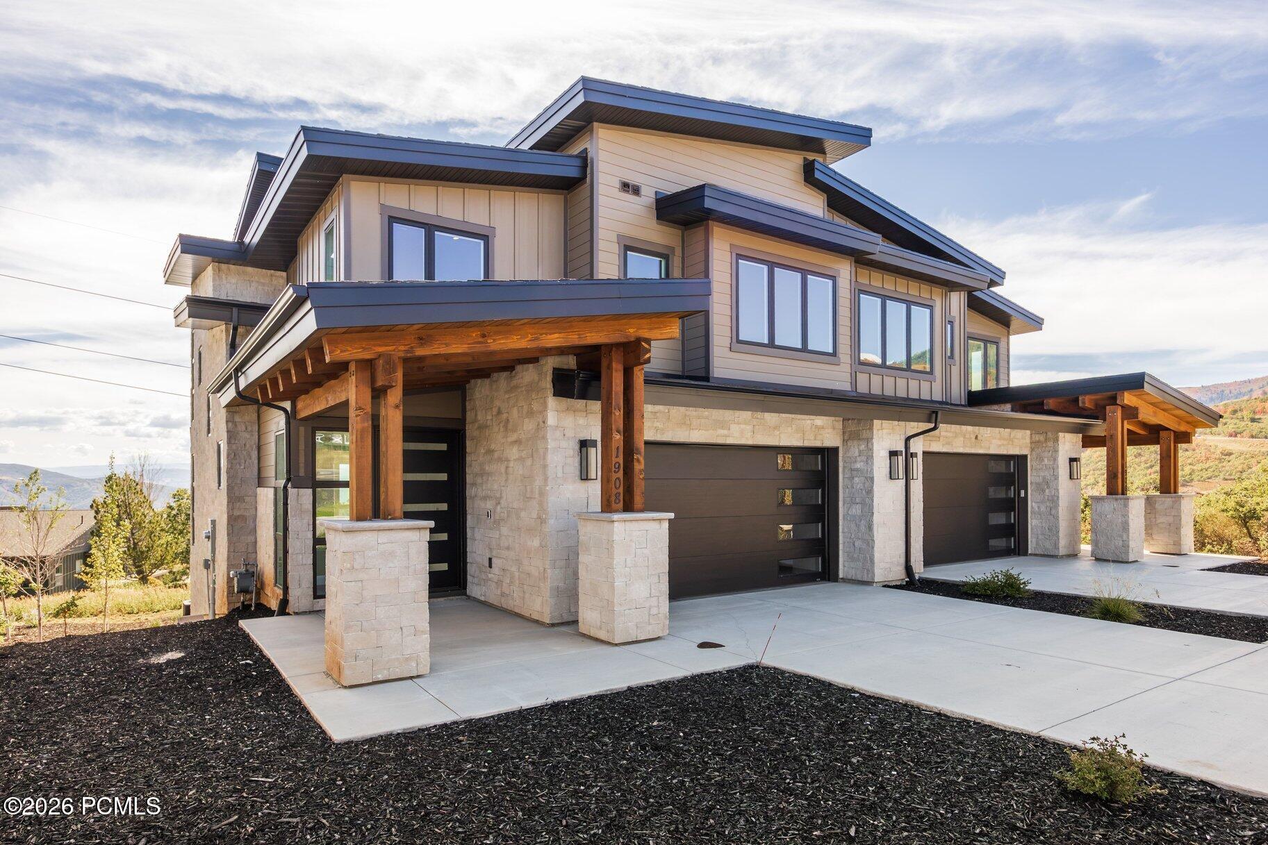 Modern two-story home with stone walls, timber porch supports, and three dark garage doors.