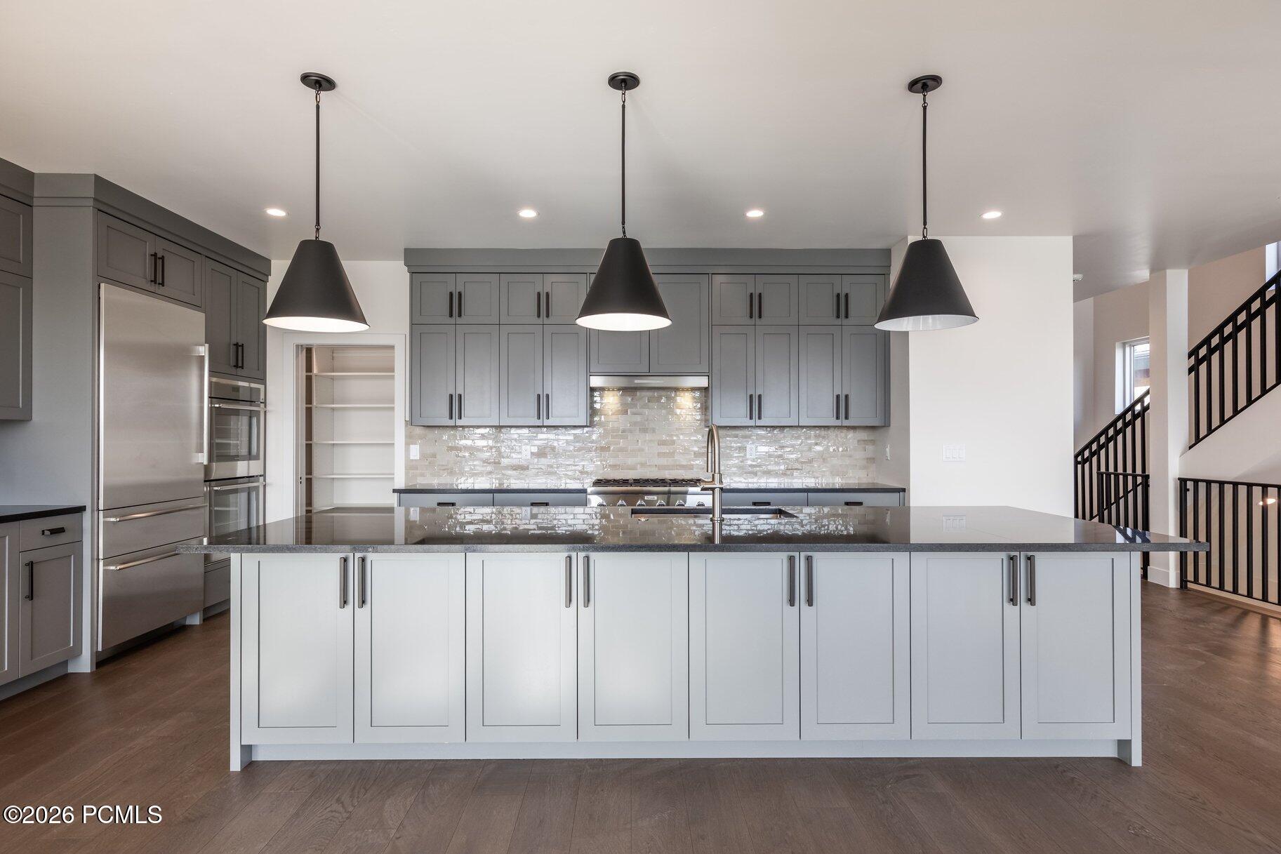 Modern kitchen with a large island, gray cabinets, stainless steel appliances, and three black pendant lights.