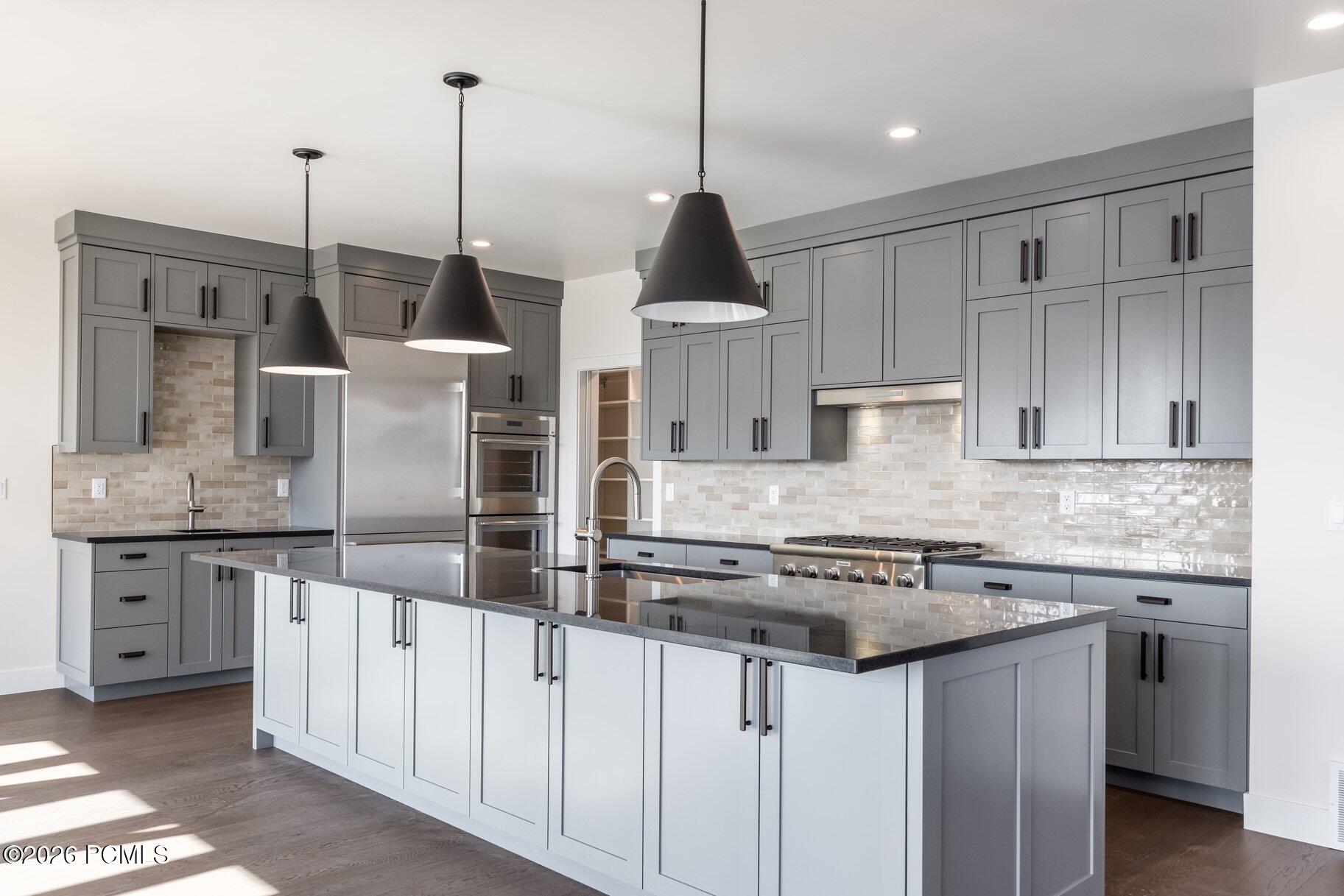 Kitchen with gray cabinets, a large island, pendant lights, and stainless steel appliances.