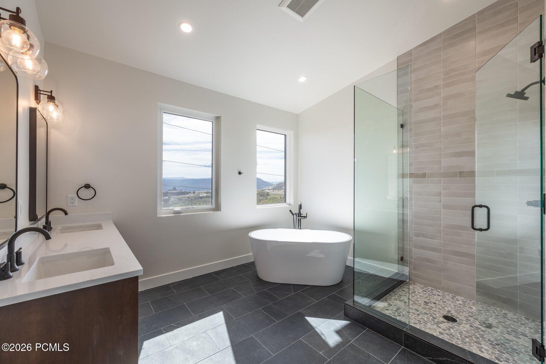 Modern bathroom with a freestanding tub, glass shower, double vanity, and mountain views.