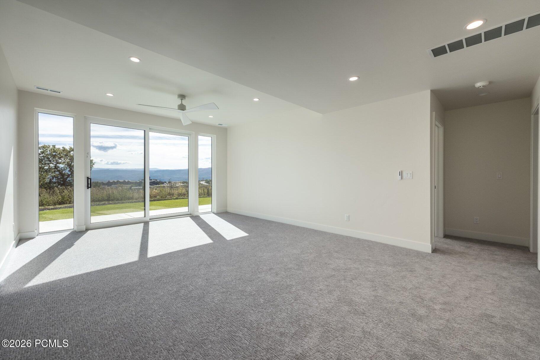Empty carpeted room with large glass doors overlooking green lawn and distant hills.