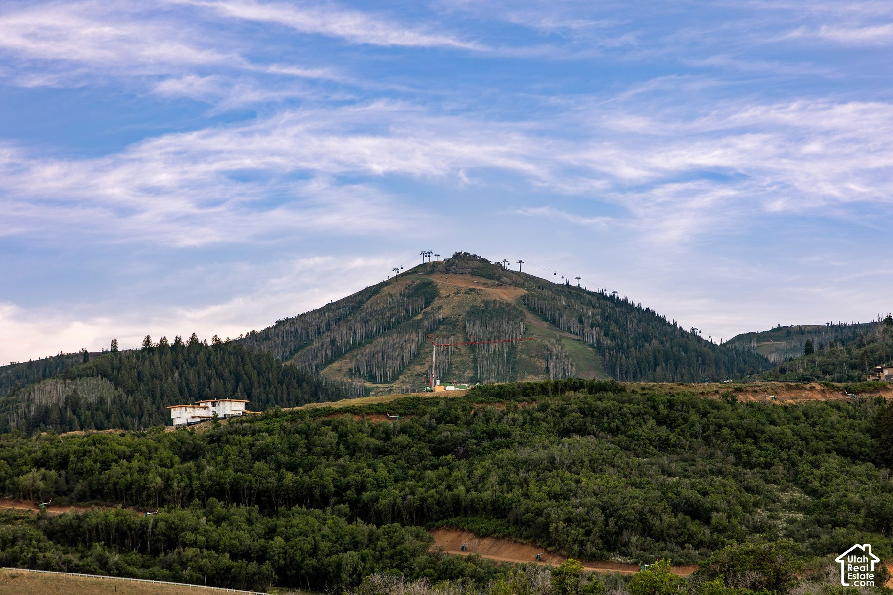 Mountain hillside with ski lifts and a construction crane above wooded terrain.