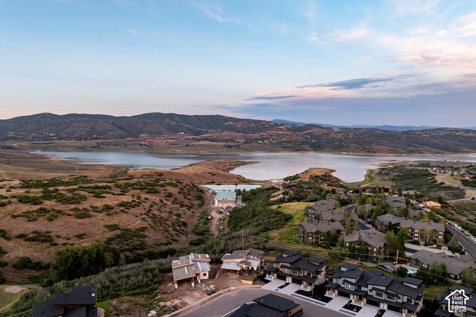 Aerial view of homes under construction beside a reservoir, with hills and mountains beyond.