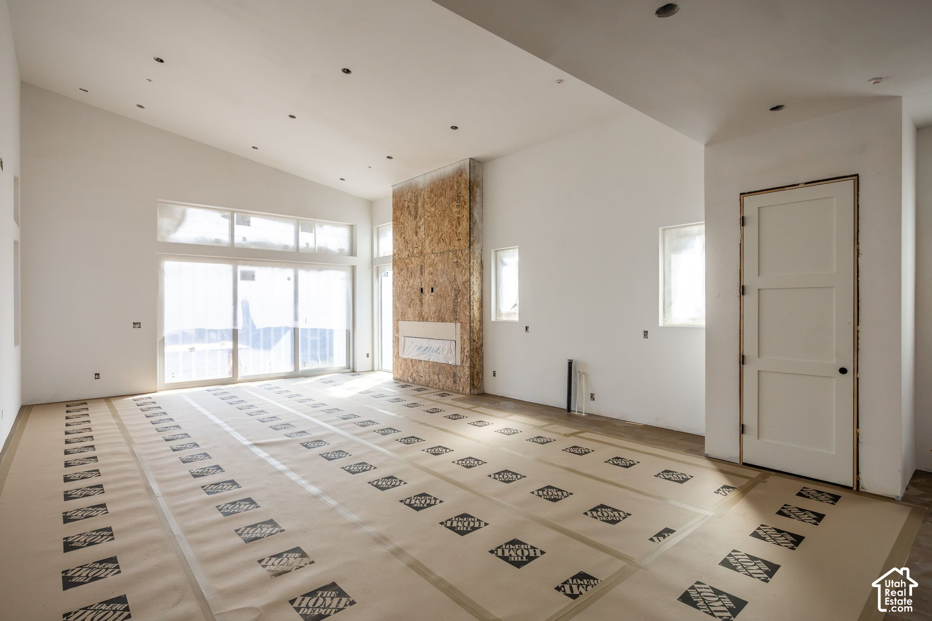 Unfinished living room with tall windows, a wood-panel fireplace surround, and protective floor covering.