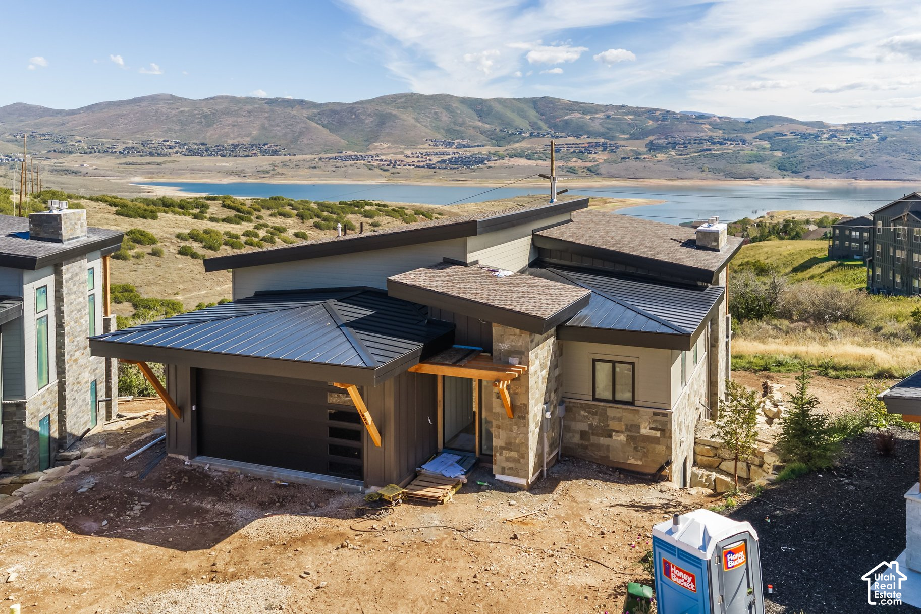 Modern home under construction overlooking a reservoir and mountain hills.