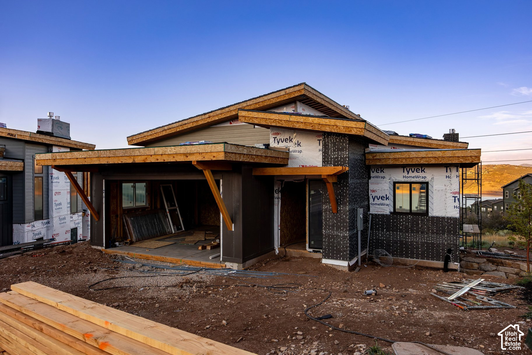 Modern home under construction with layered angular roofs and exposed house wrap.