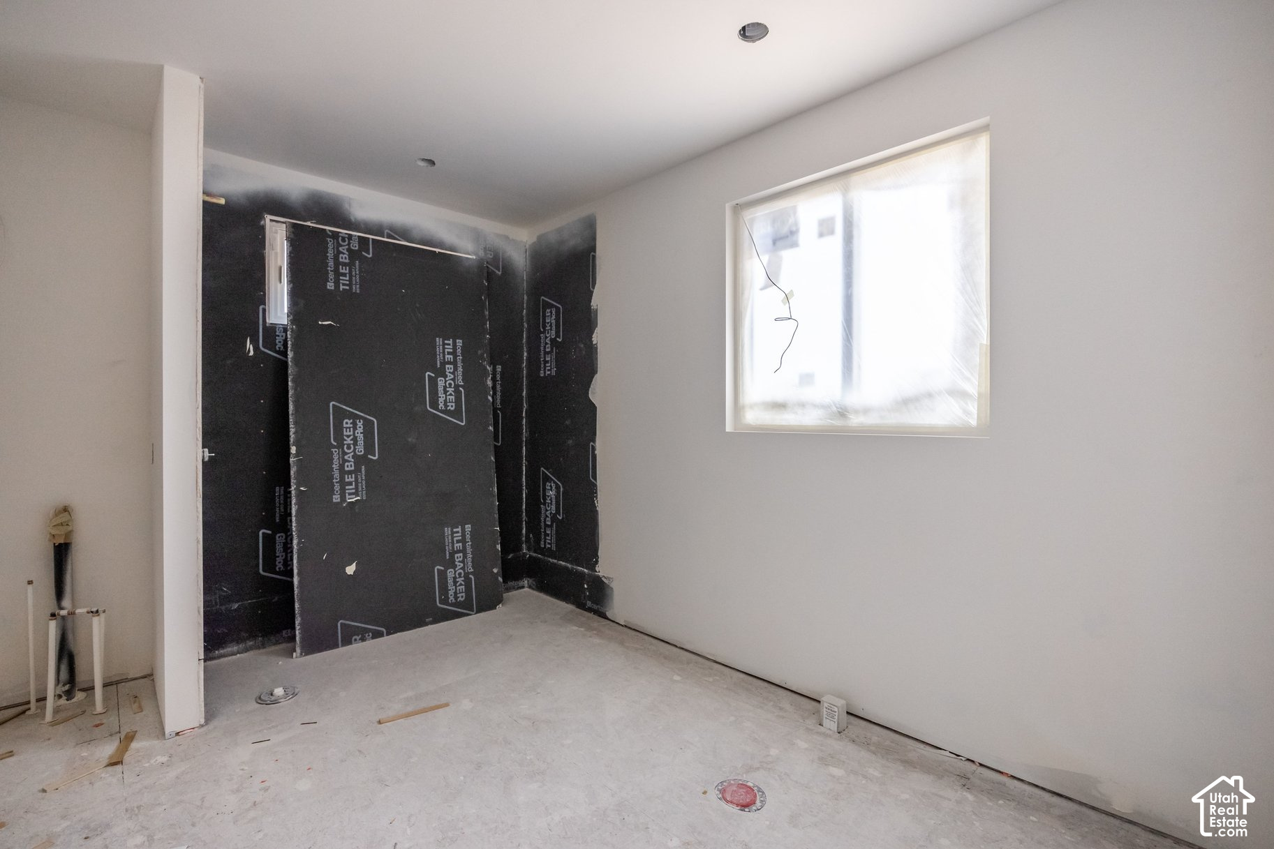 Unfinished bathroom with black shower backer panels and a plastic-covered window.