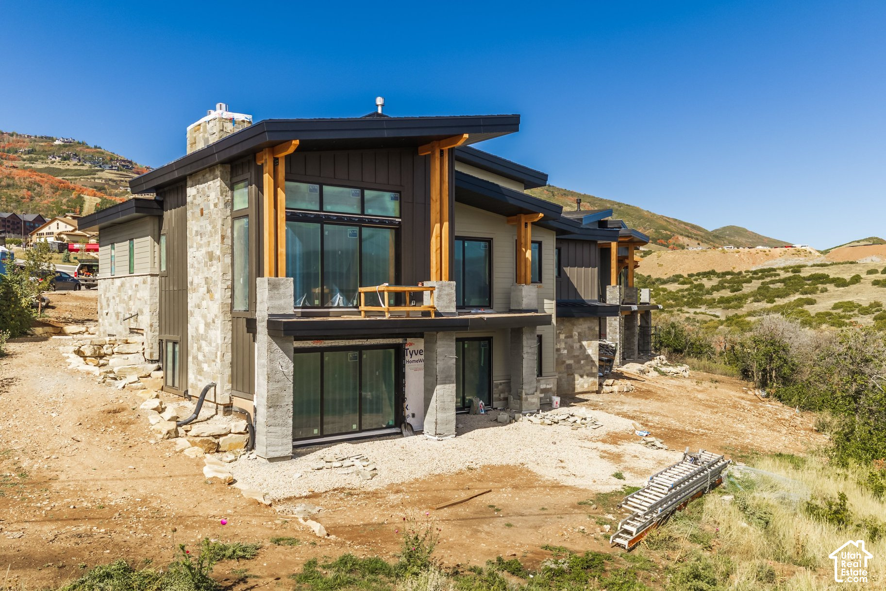 Modern home under construction with stone cladding and timber accents, set against autumn hills.