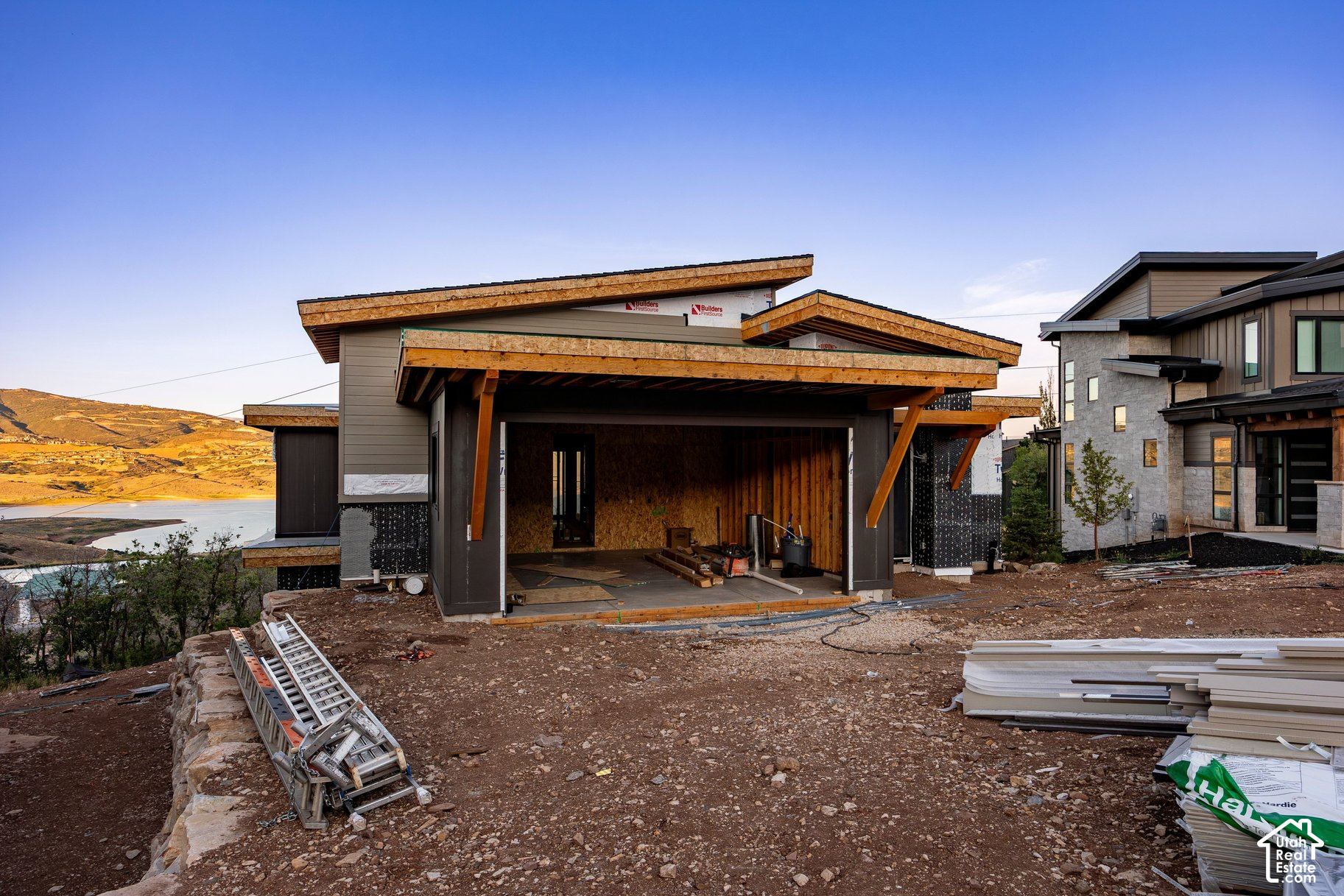 Modern home under construction on a hillside, with a lake and mountains in the background.