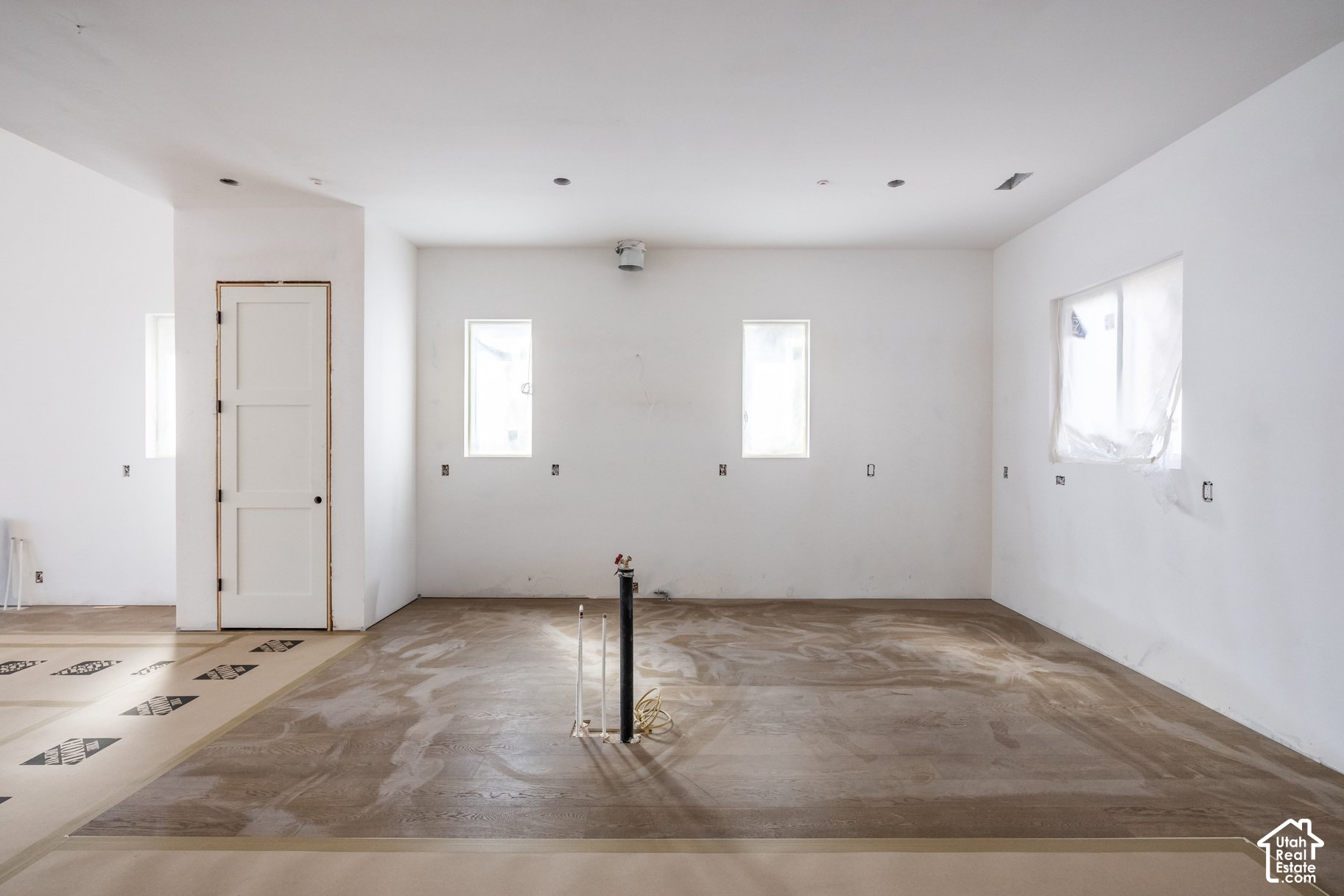 Unfinished kitchen with exposed plumbing, bare walls, and a window covered in plastic.