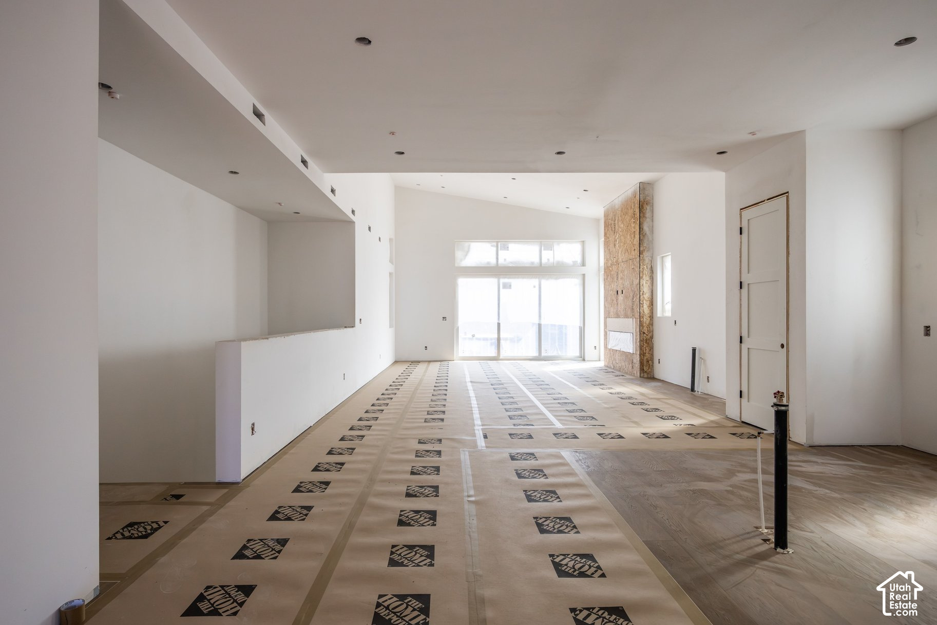 Unfinished open-plan living room with large windows, a stone fireplace, and protective floor covering.