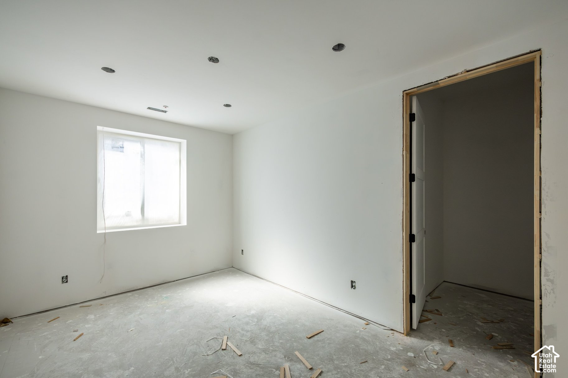 Unfinished room with a window, bare concrete floor, and untrimmed doorway.