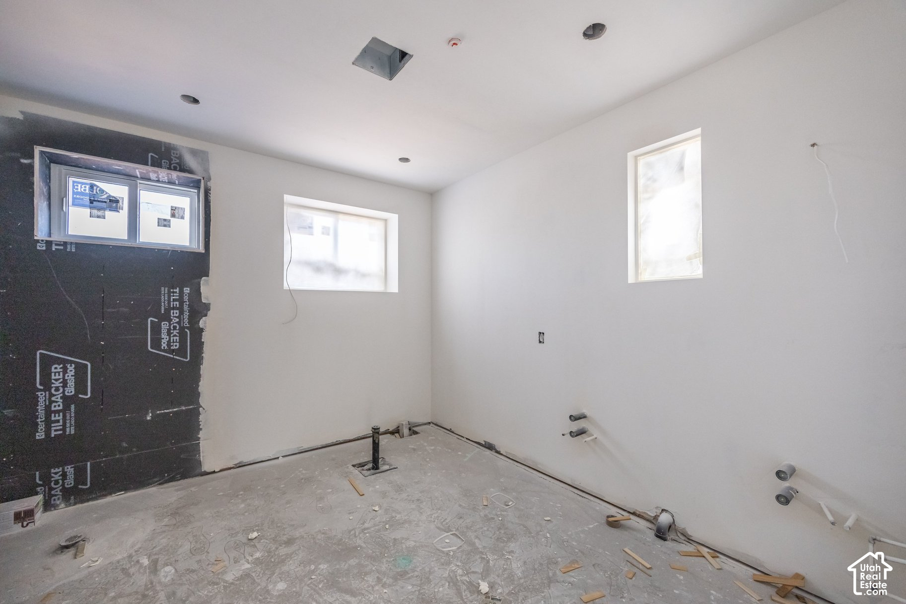 Unfinished bathroom with exposed plumbing, tile backer board, and two windows.