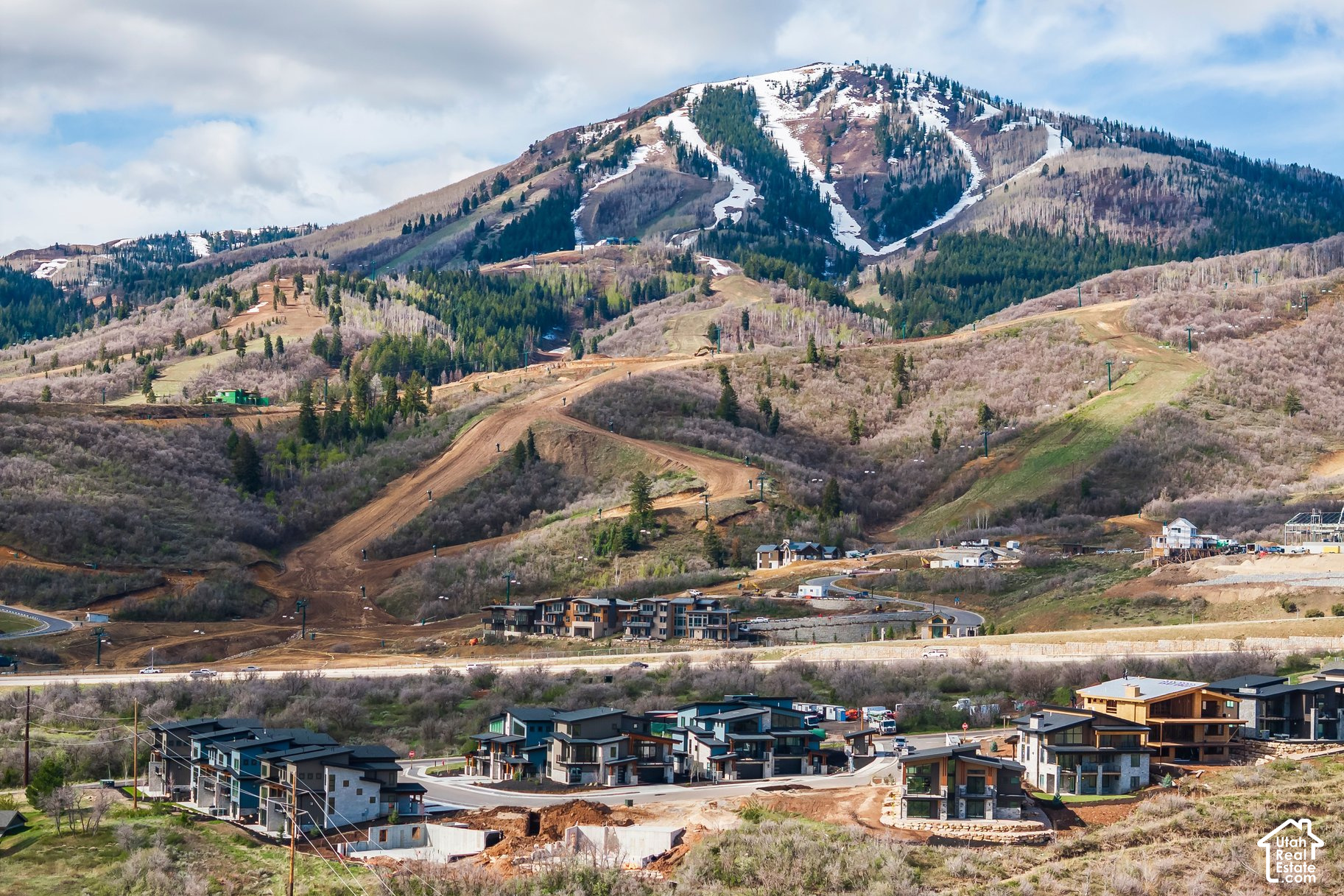 Hillside homes and construction beneath a snow-dusted mountain with ski runs.