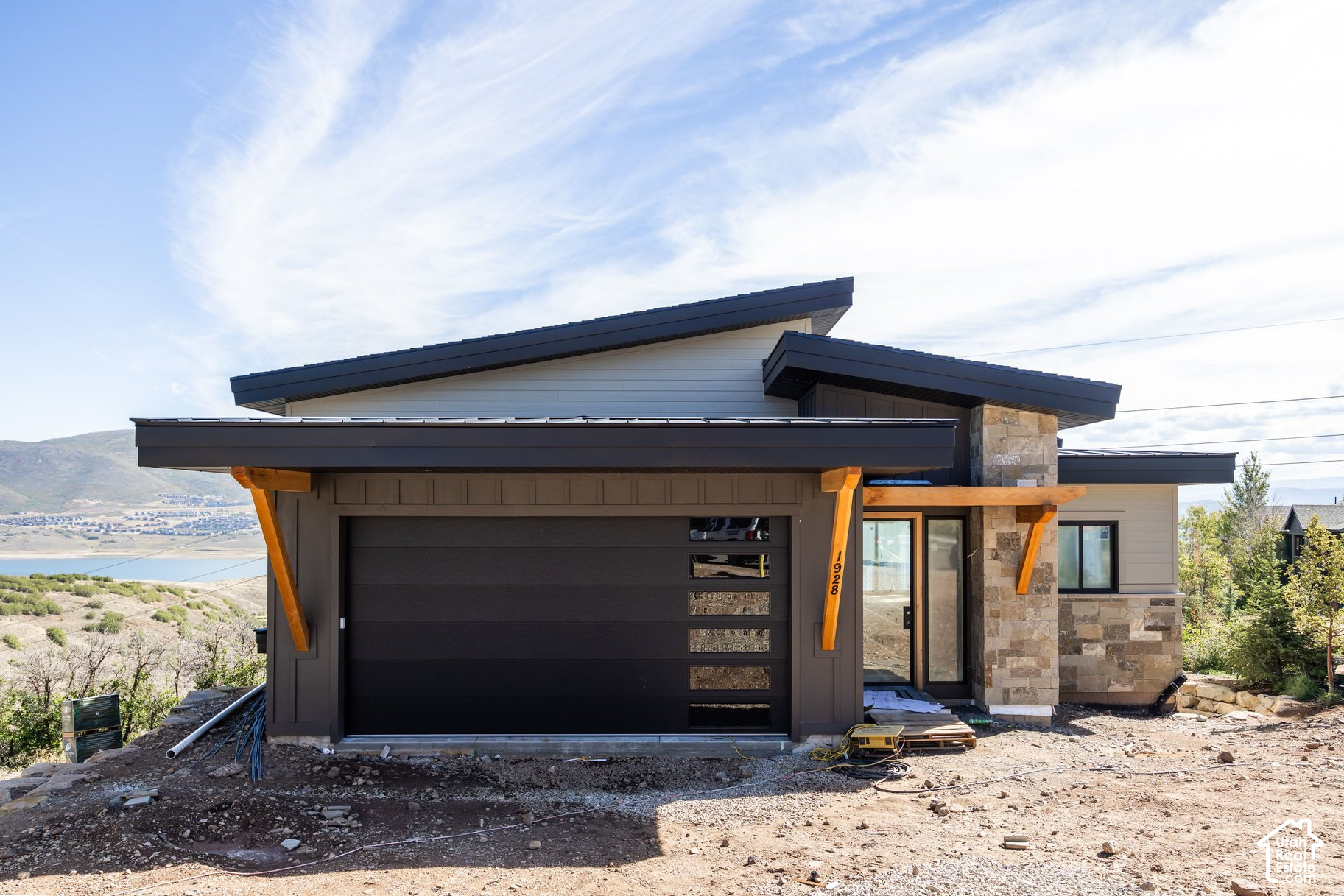 Modern home under construction with a dark garage, stone accents, and a lake and mountain view.