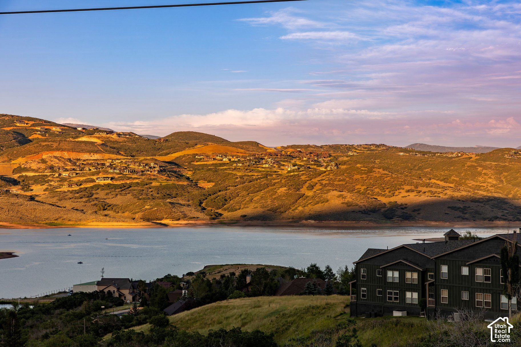 Lake and rolling hills dotted with homes, viewed past houses in the foreground at golden hour.
