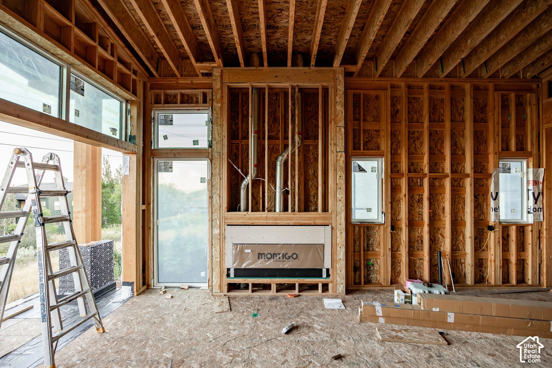 Unfinished home interior with exposed framing, large windows, and a fireplace insert.