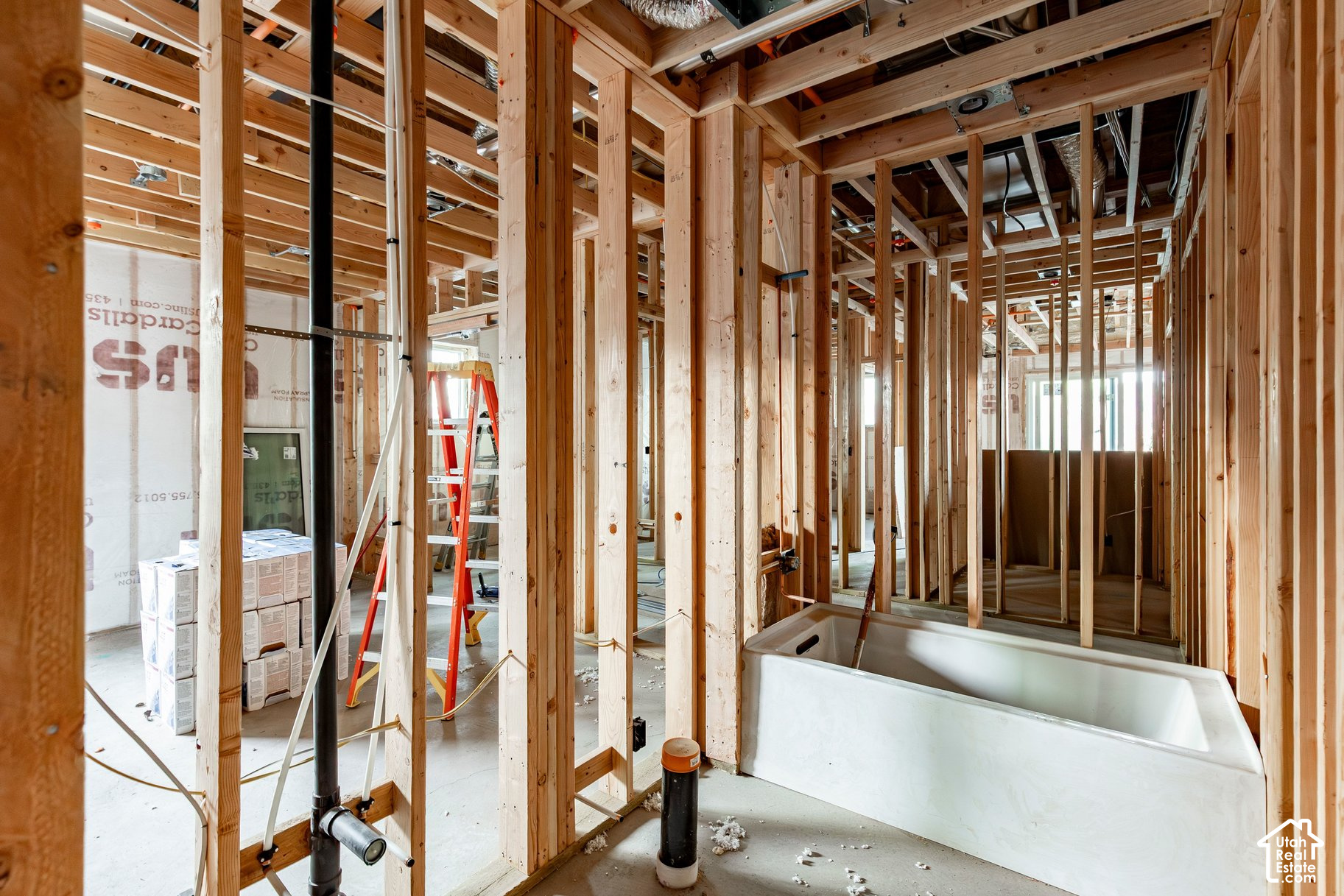 Unfinished bathroom with exposed wood framing, visible plumbing, and a white bathtub.