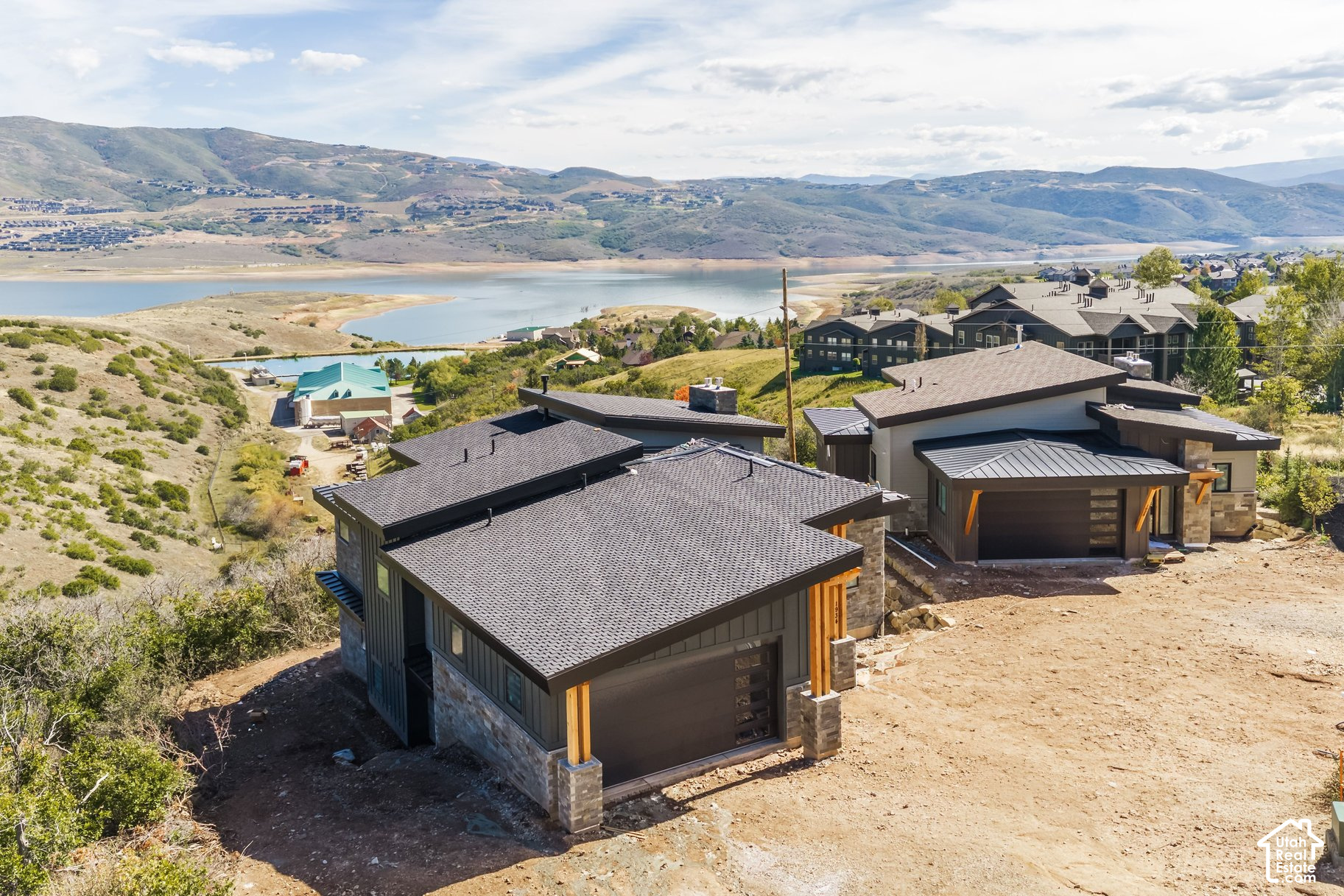 Modern hillside home overlooking a lake and mountains, with unfinished landscaping.