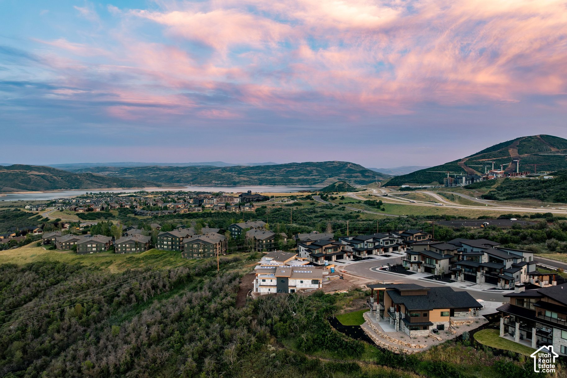 Aerial view of modern homes overlooking a lake and mountain ranges at dusk.