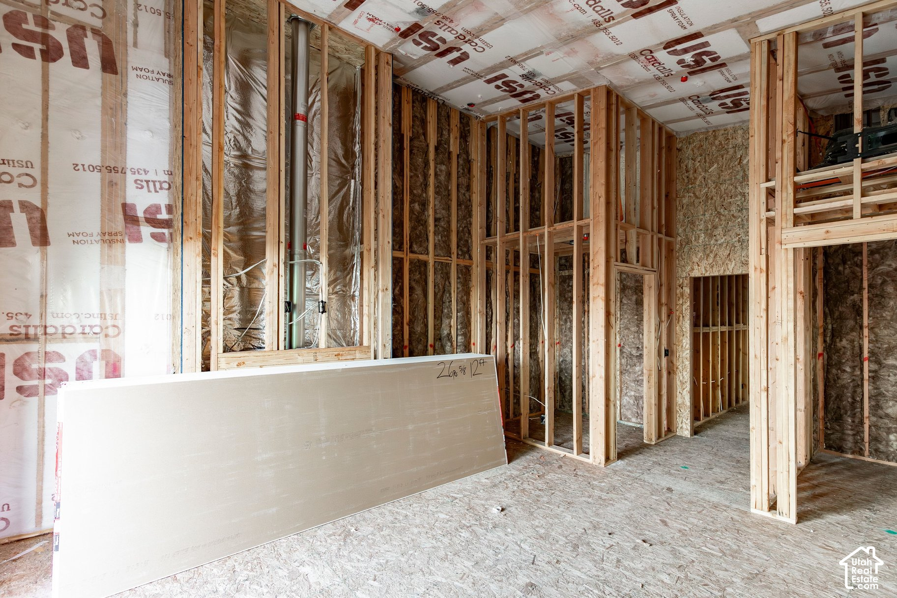 Unfinished home interior with exposed framing, insulation, ductwork, and a sheet of drywall.