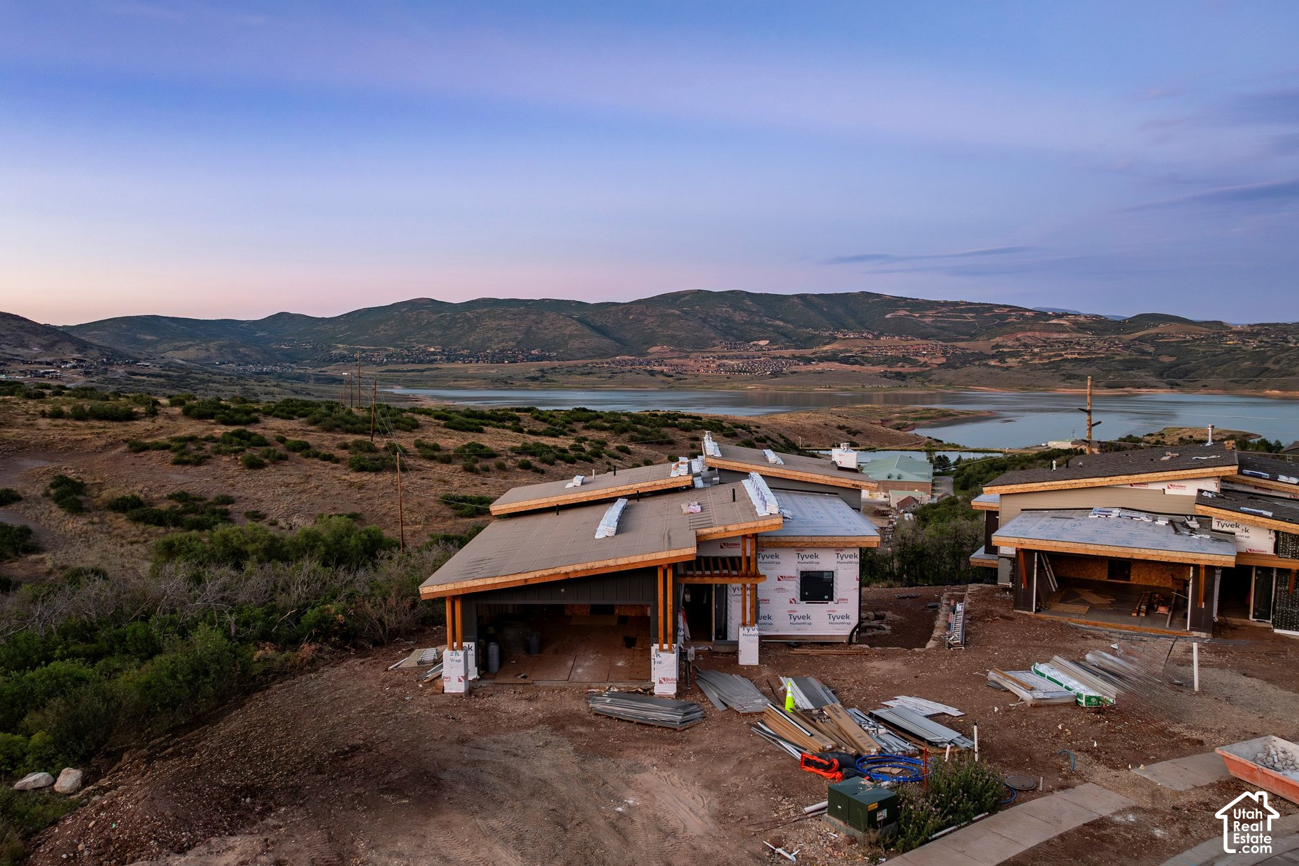 Homes under construction overlook a reservoir and mountain valley at dusk.