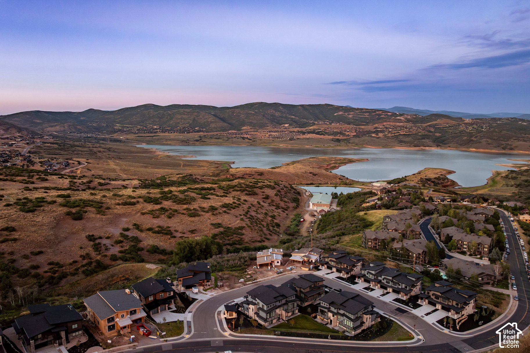 Aerial view of homes beside a lake, with rolling mountains in the distance at dusk.