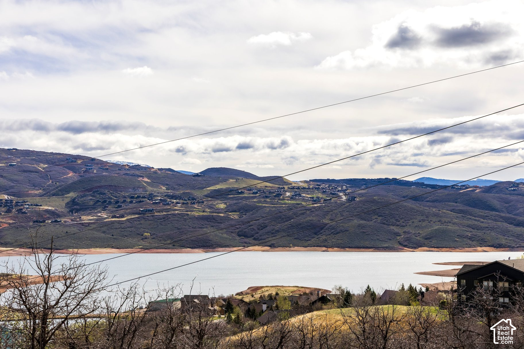 Lake and rolling hills dotted with homes, viewed past foreground houses and utility lines.