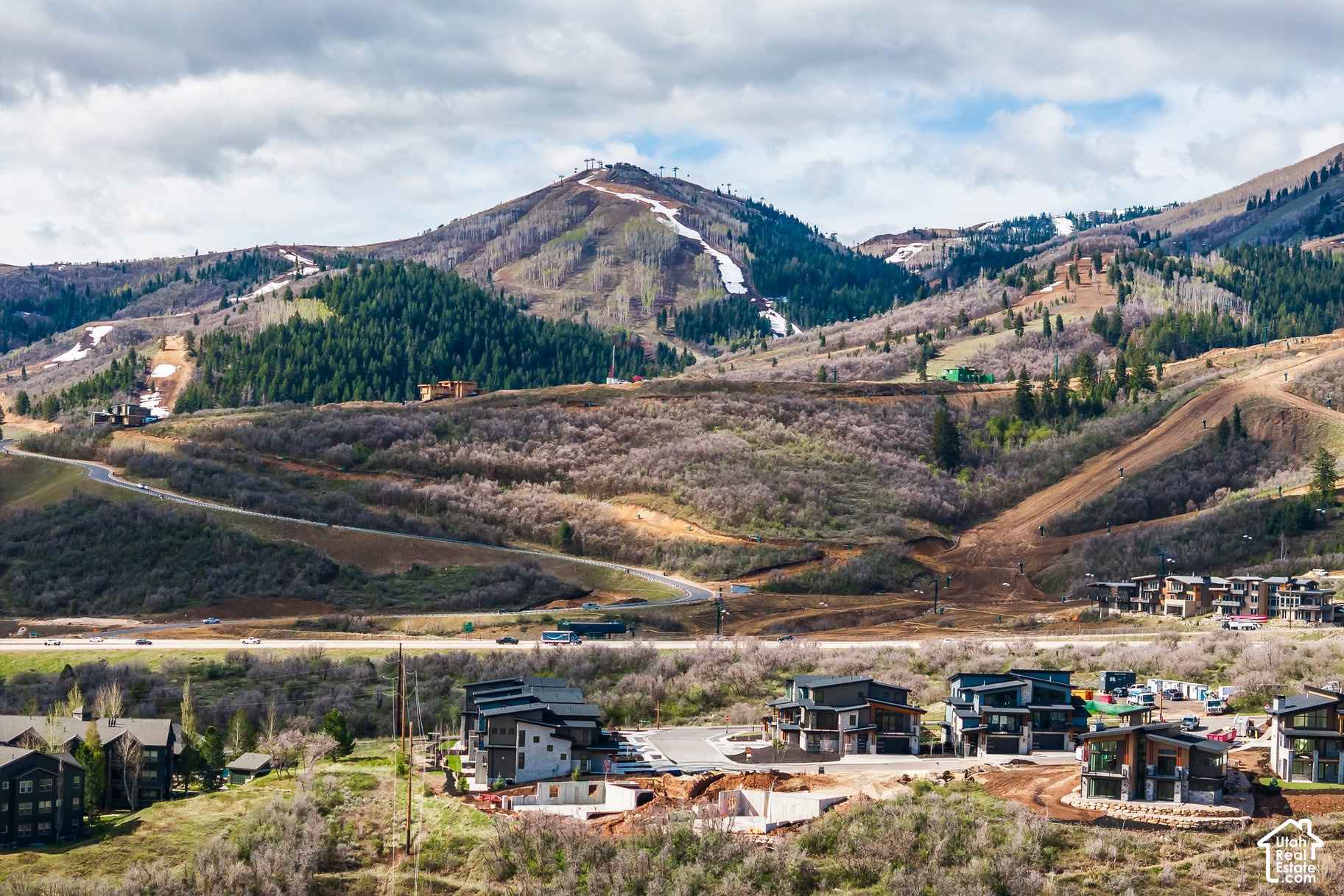 Developing neighborhood and construction sites below forested mountains with ski runs.