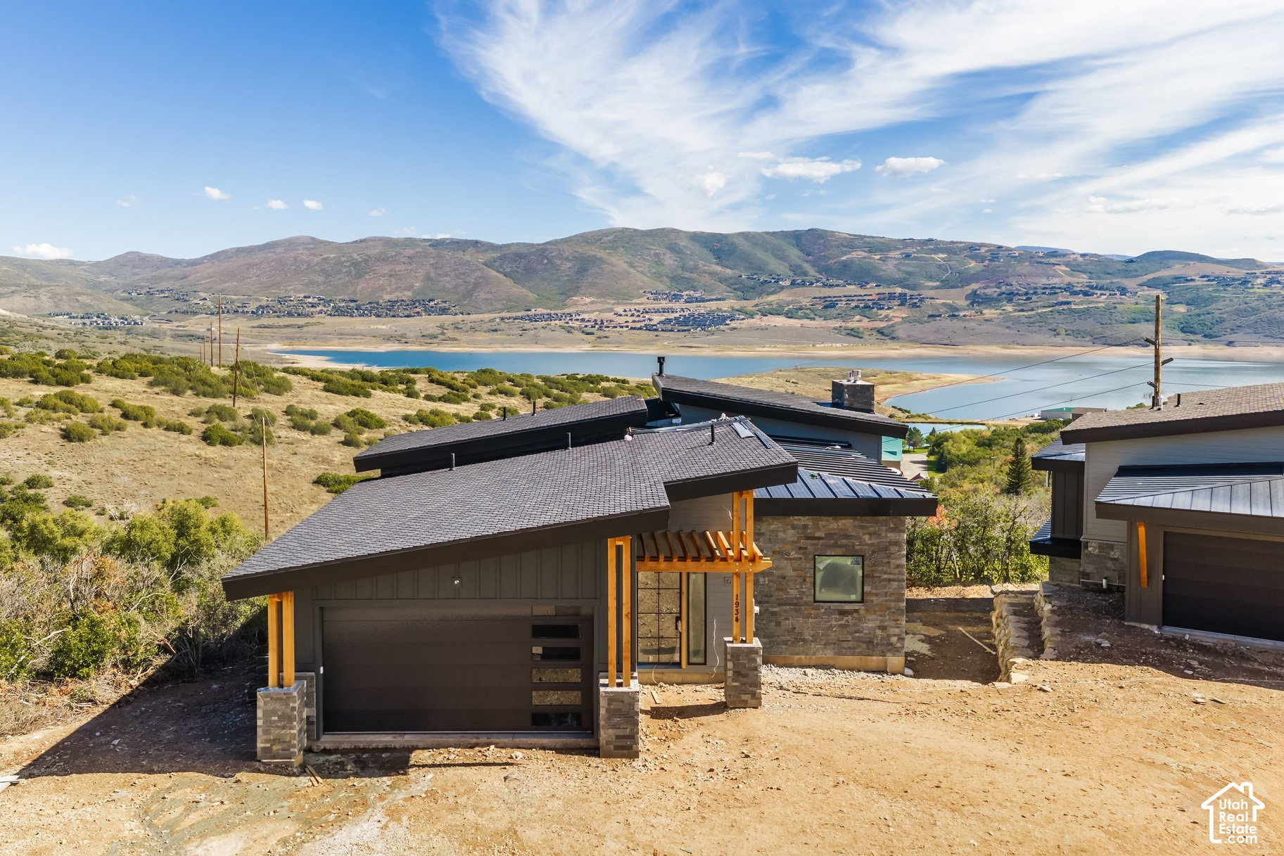 Modern home with stone accents overlooks a lake and rolling hills.