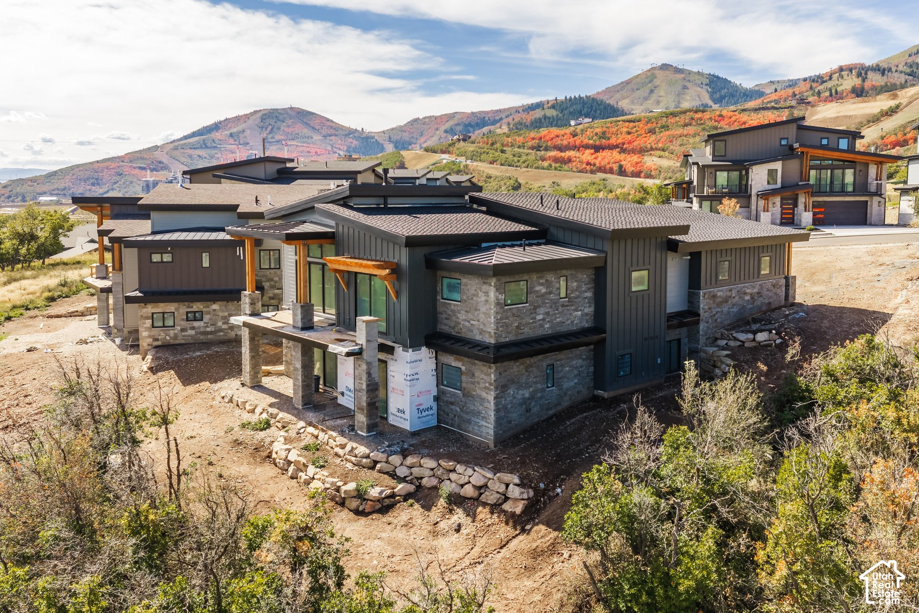 Modern mountain home under construction on a rocky slope, with autumn hills behind it.