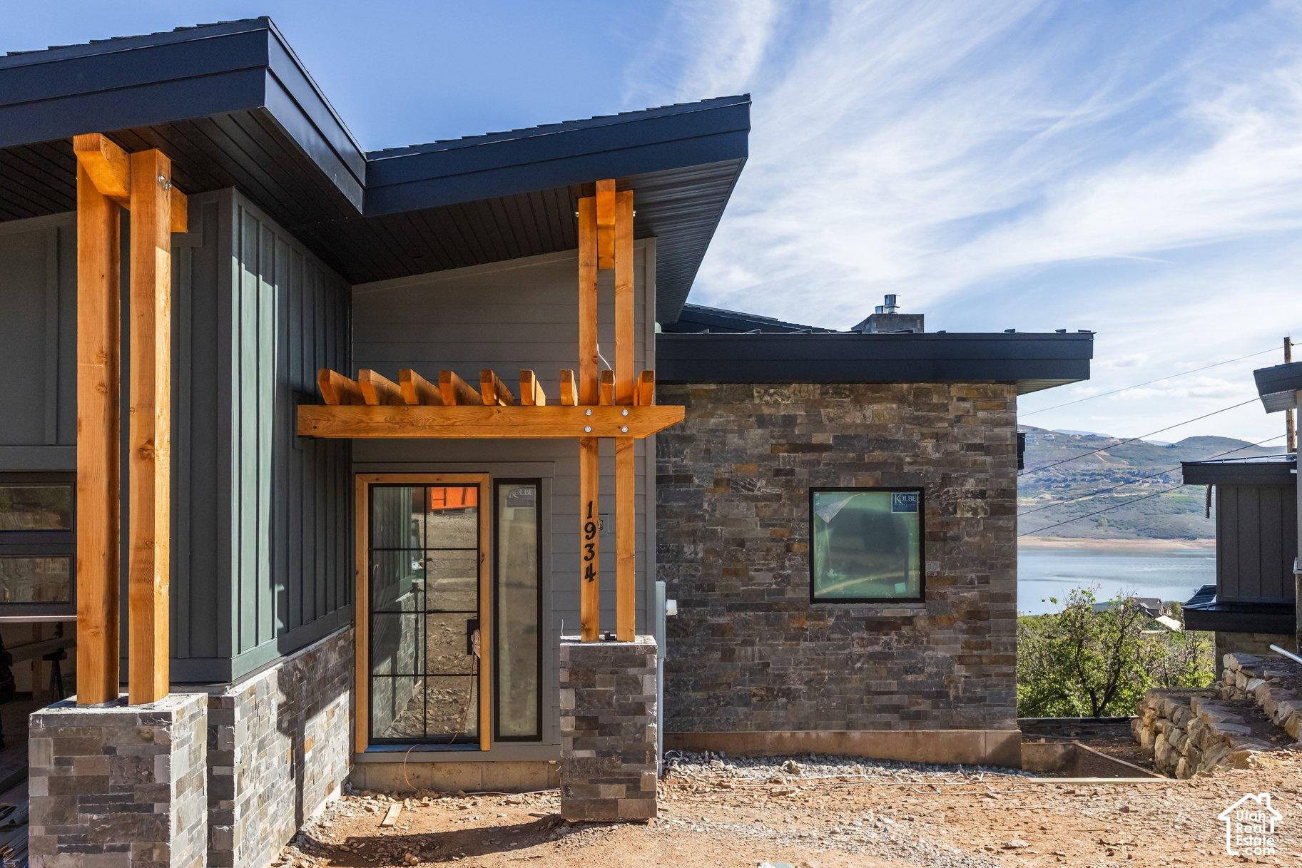 Modern stone-and-timber house under construction, with a lake and mountain view.