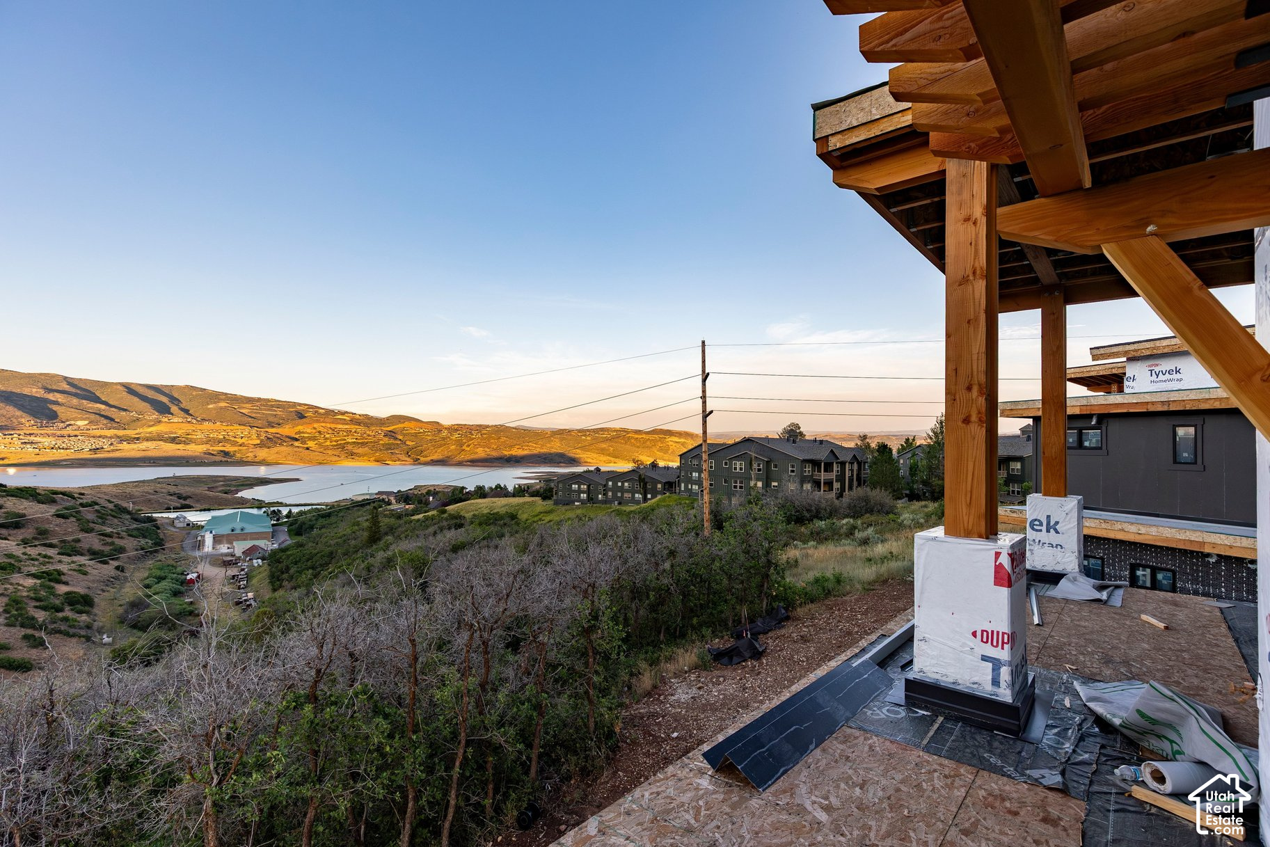 Construction site with exposed timber framing overlooks a lake and sunlit hills.