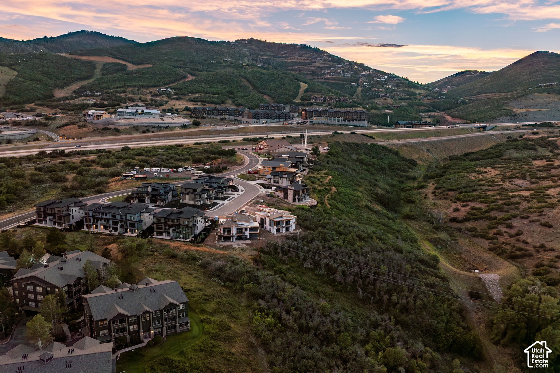 Hillside neighborhood with modern homes and winding roads beneath mountain ridges at sunset.