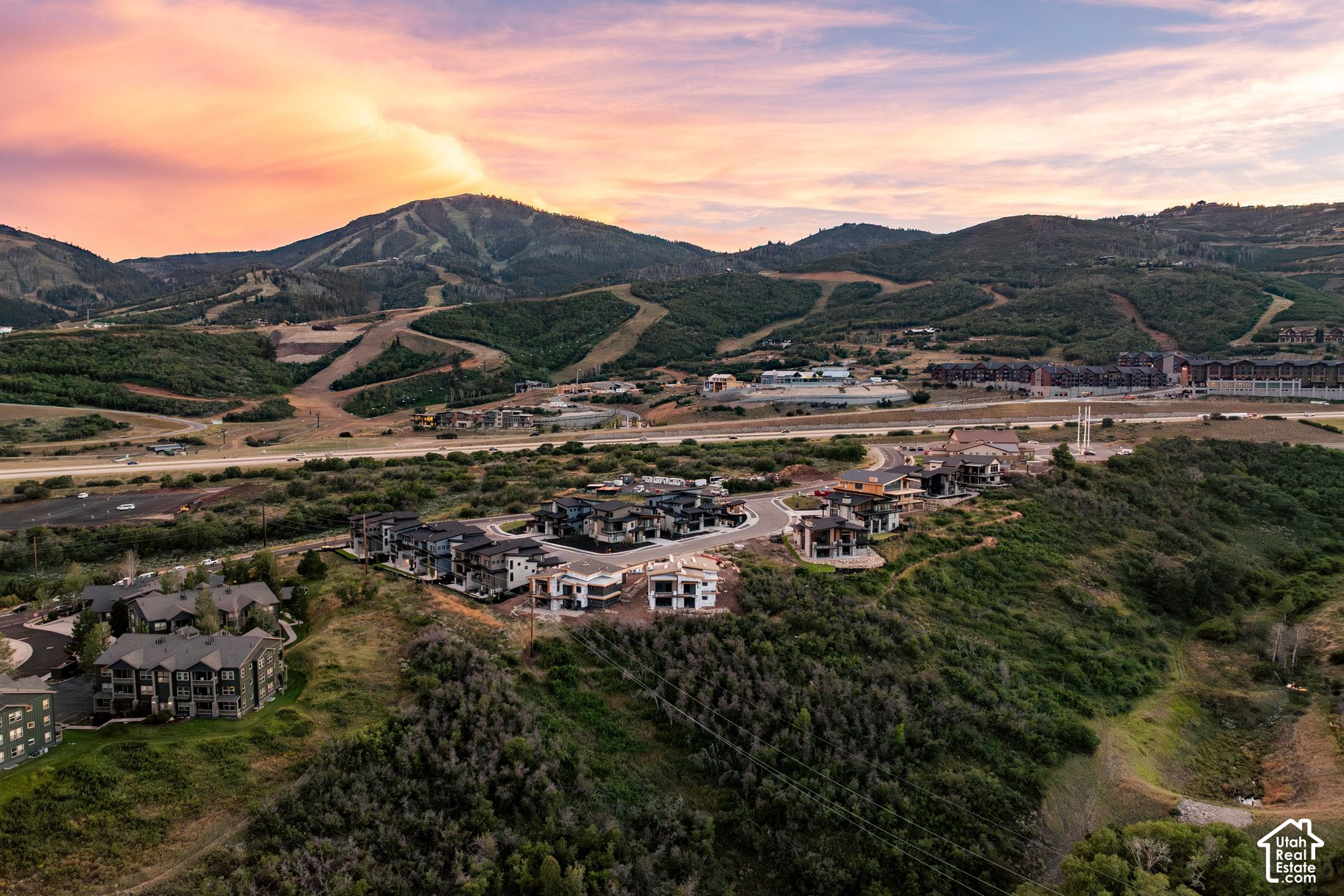 Aerial view of homes in a mountain valley beneath a pink sunset sky.