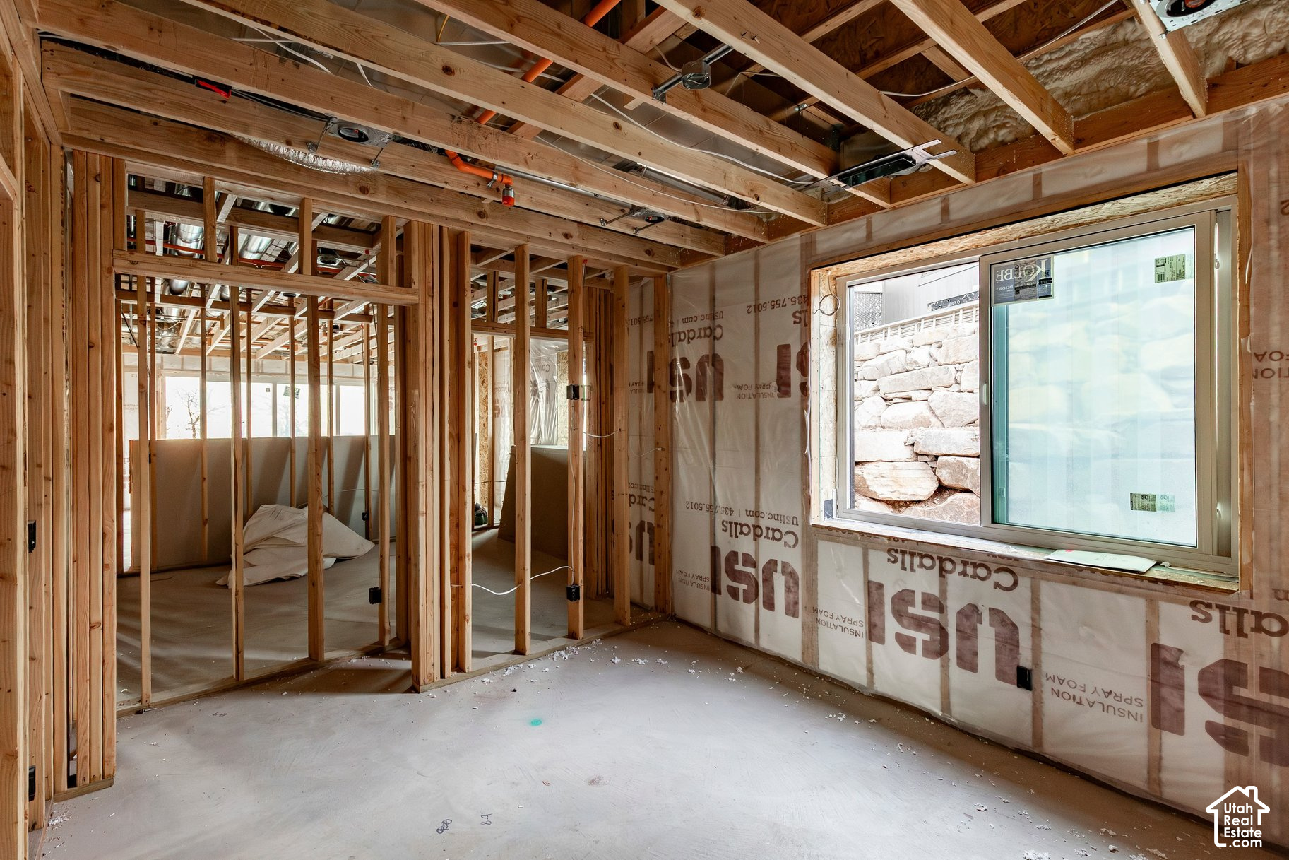 Unfinished room with exposed wood framing, insulation, and a large window facing a stone retaining wall.