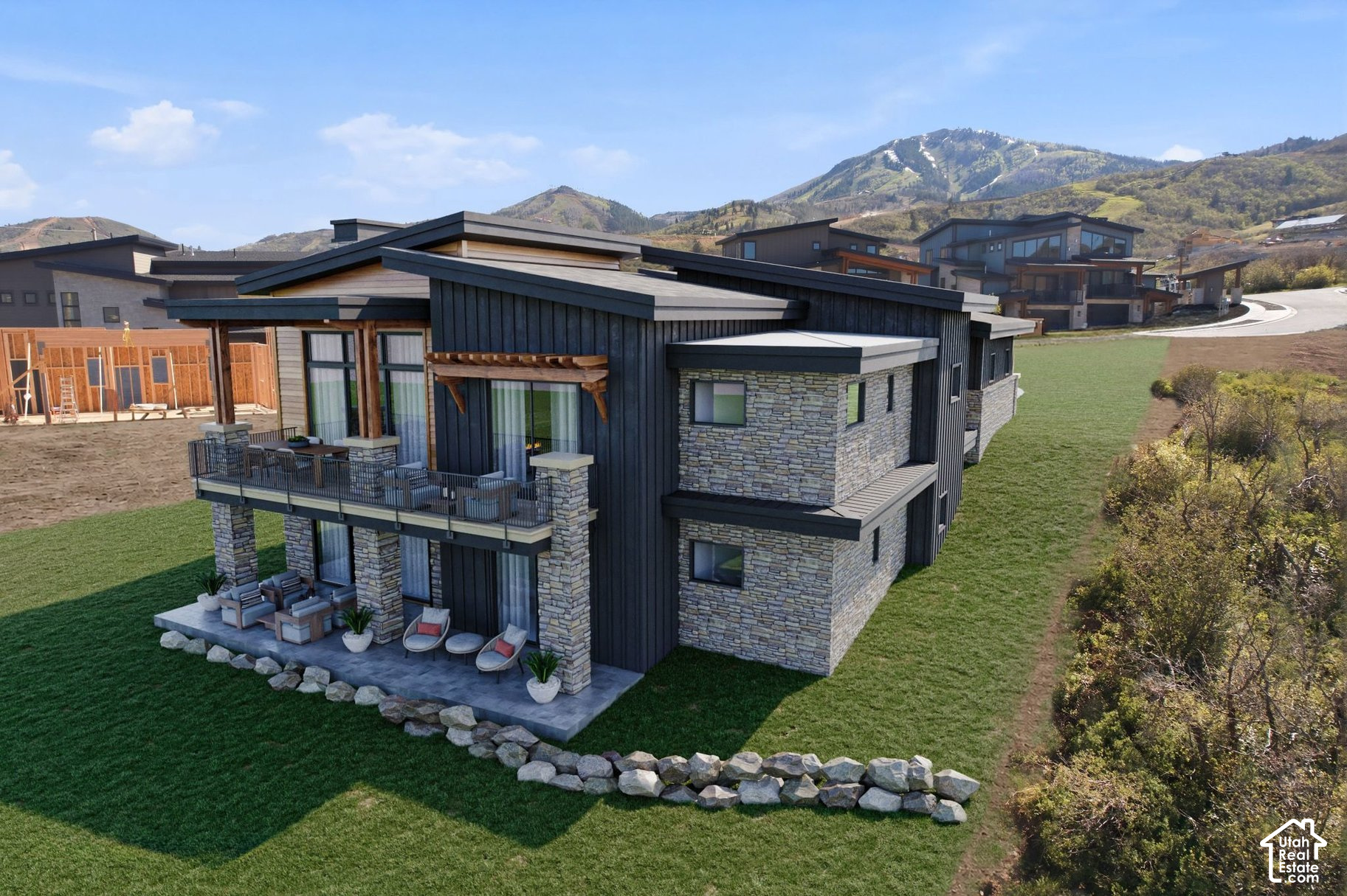 Modern two-story home with dark siding, stone walls, and balconies, set against a mountain backdrop.