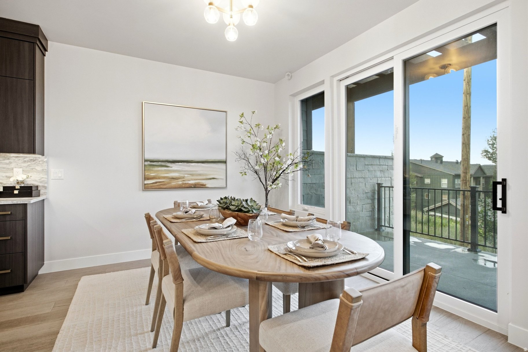 Staged dining area with an oval wood table, dark cabinetry, and sliding glass doors to a balcony.