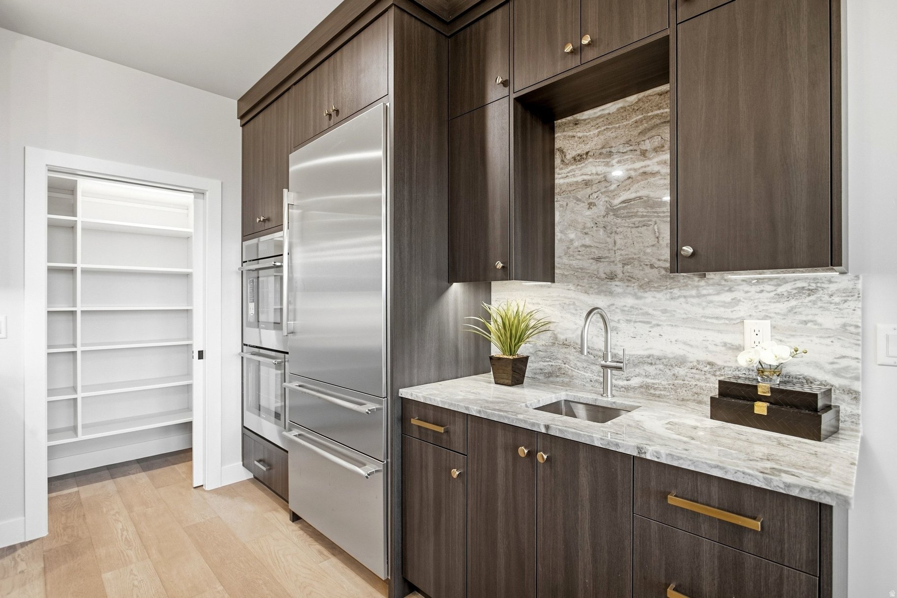 Modern kitchen with dark wood cabinets, stainless appliances, veined stone counters, and an open pantry.