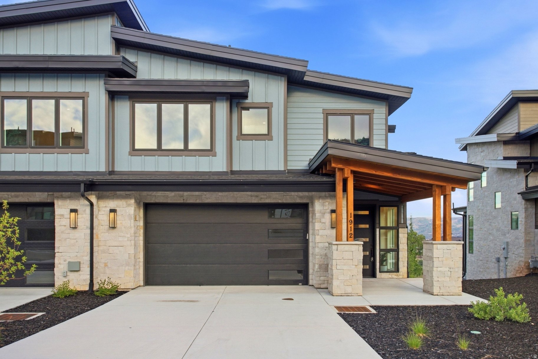 Modern two-story home with stone accents, a wide garage door, and a timber-covered entrance.