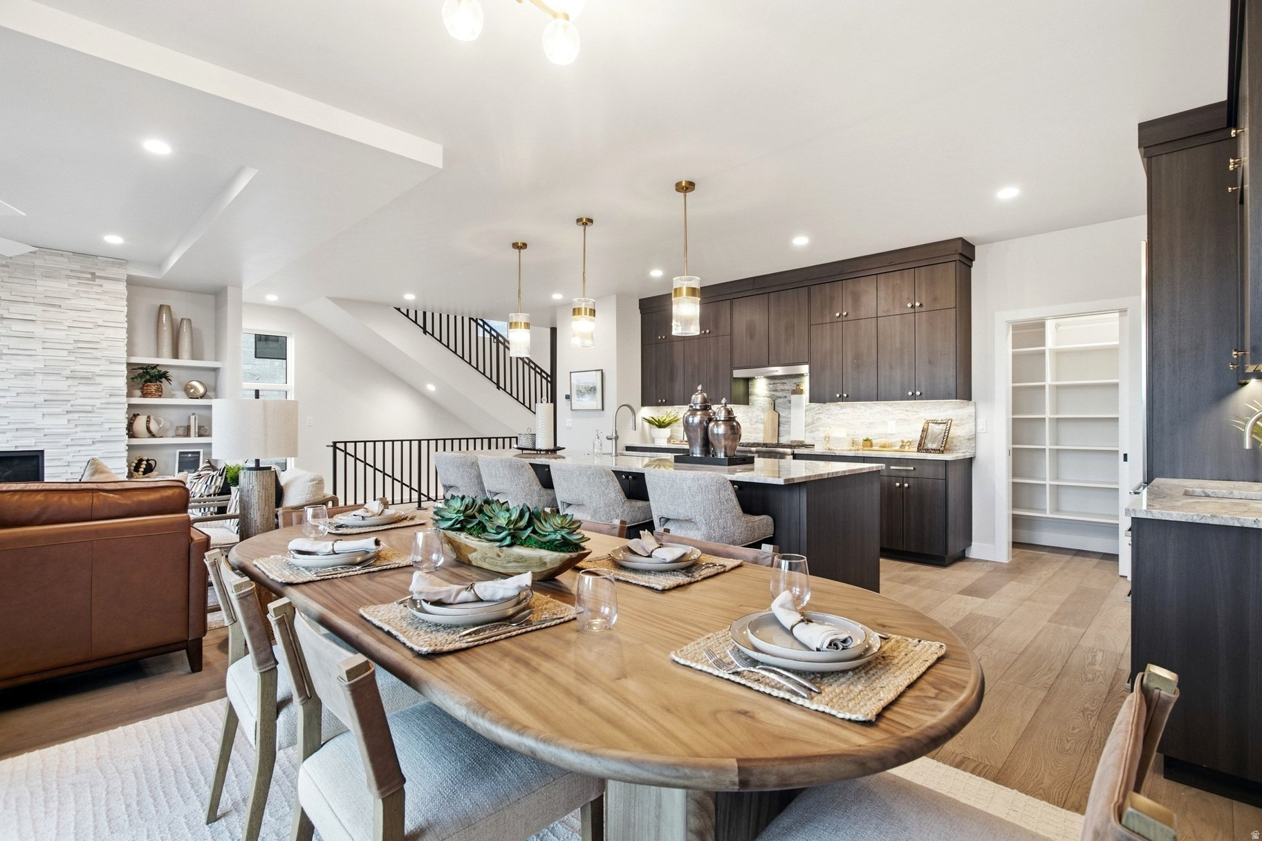 Staged kitchen and dining area with dark cabinetry, stone fireplace, and a set dining table.