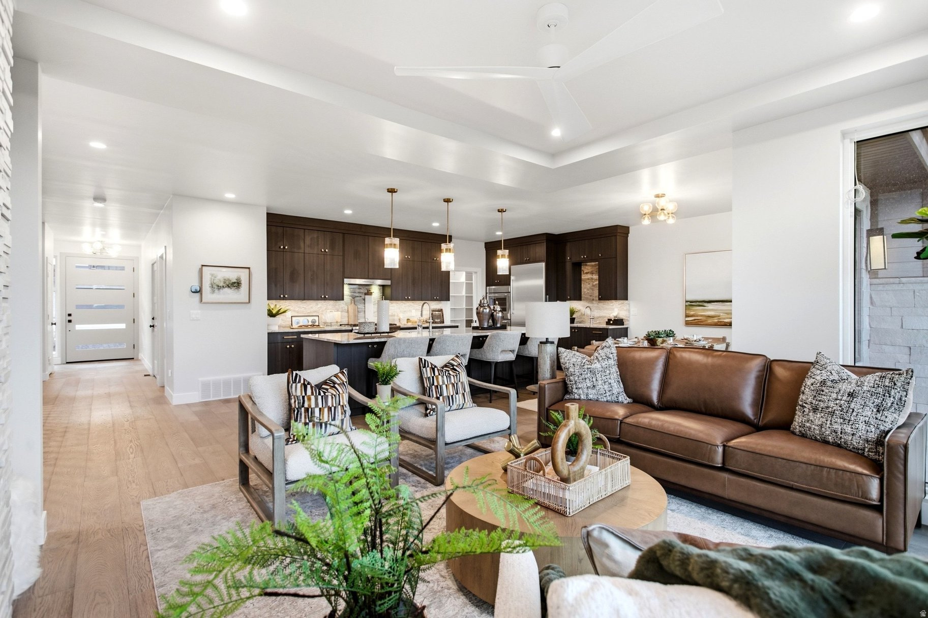 Open-plan living room and kitchen with dark cabinetry, an island, and a brown leather sofa.