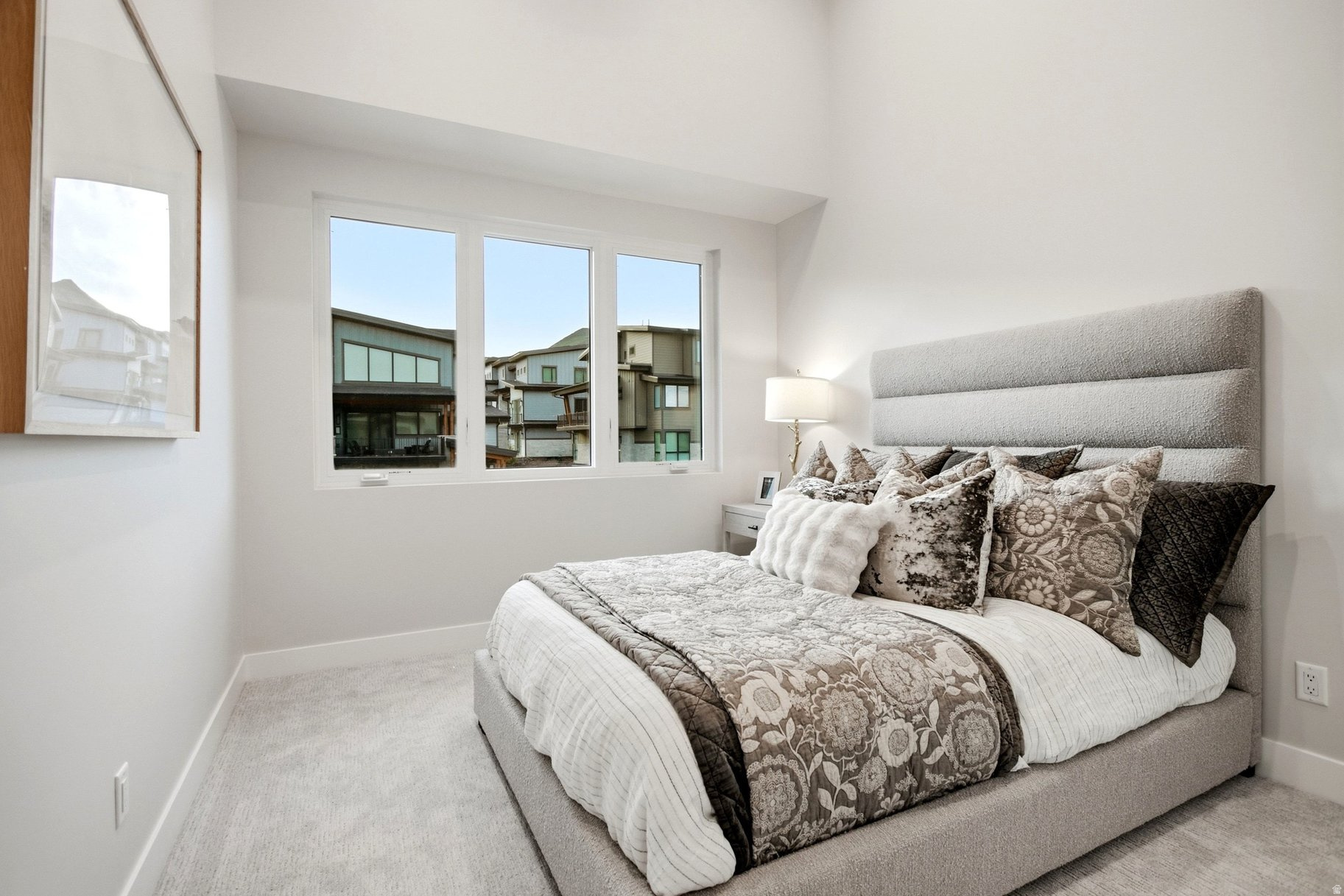 Staged bedroom with a large upholstered bed and three windows overlooking neighboring homes.