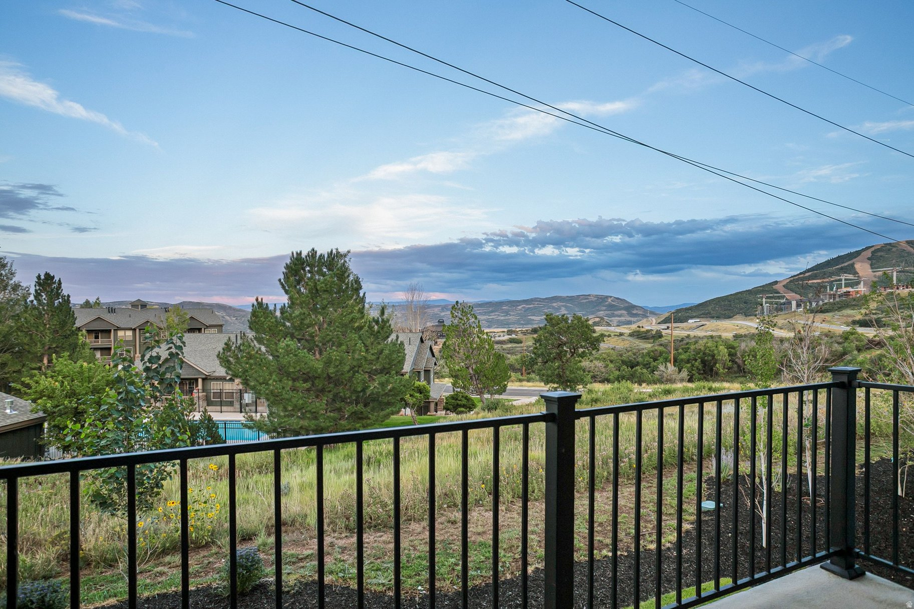 Mountain valley view from a deck, with neighboring homes, a pool, and a graded hillside.