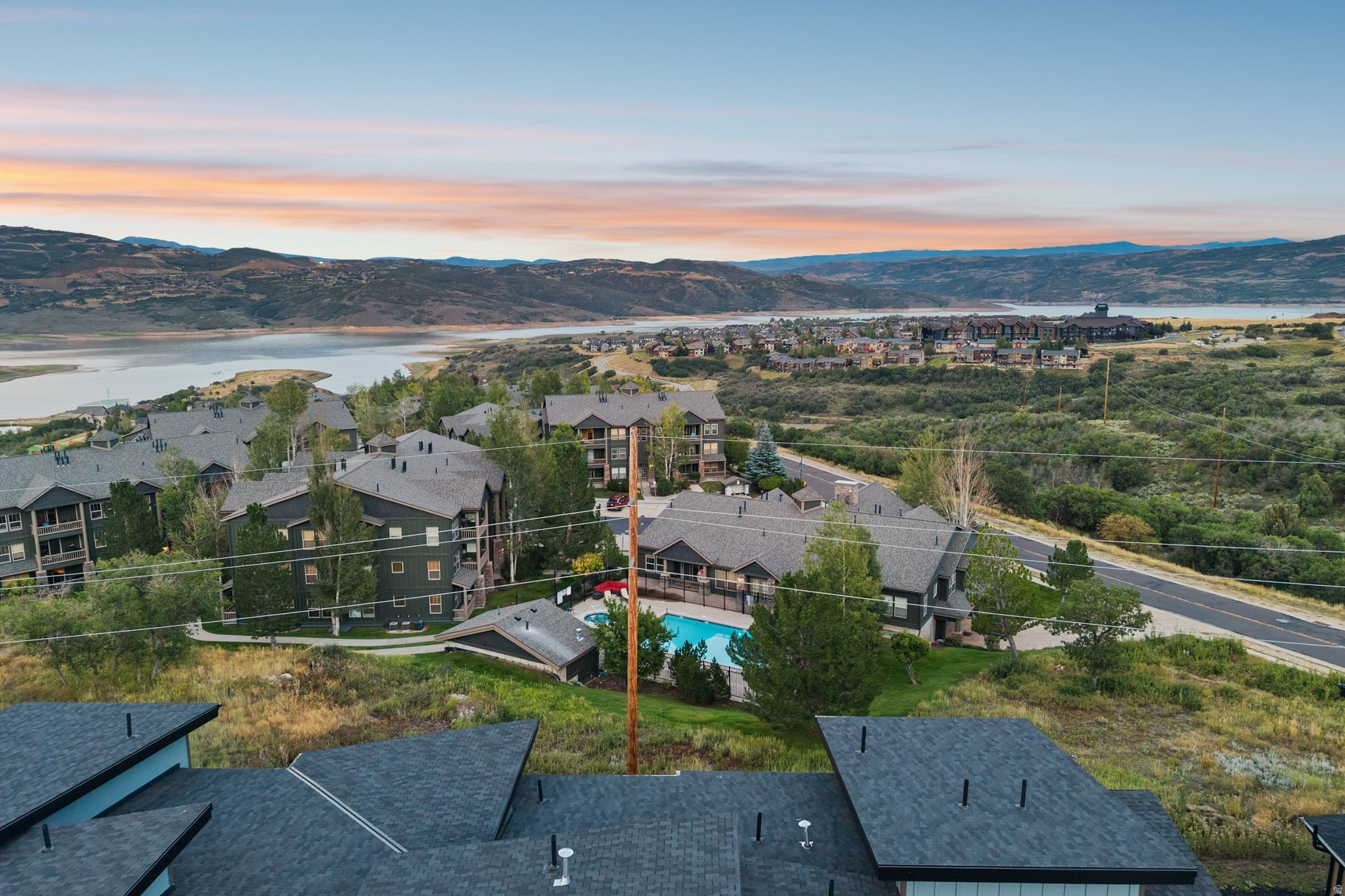 Aerial view of homes and a community pool beside a lake, with mountain ridges in the distance.
