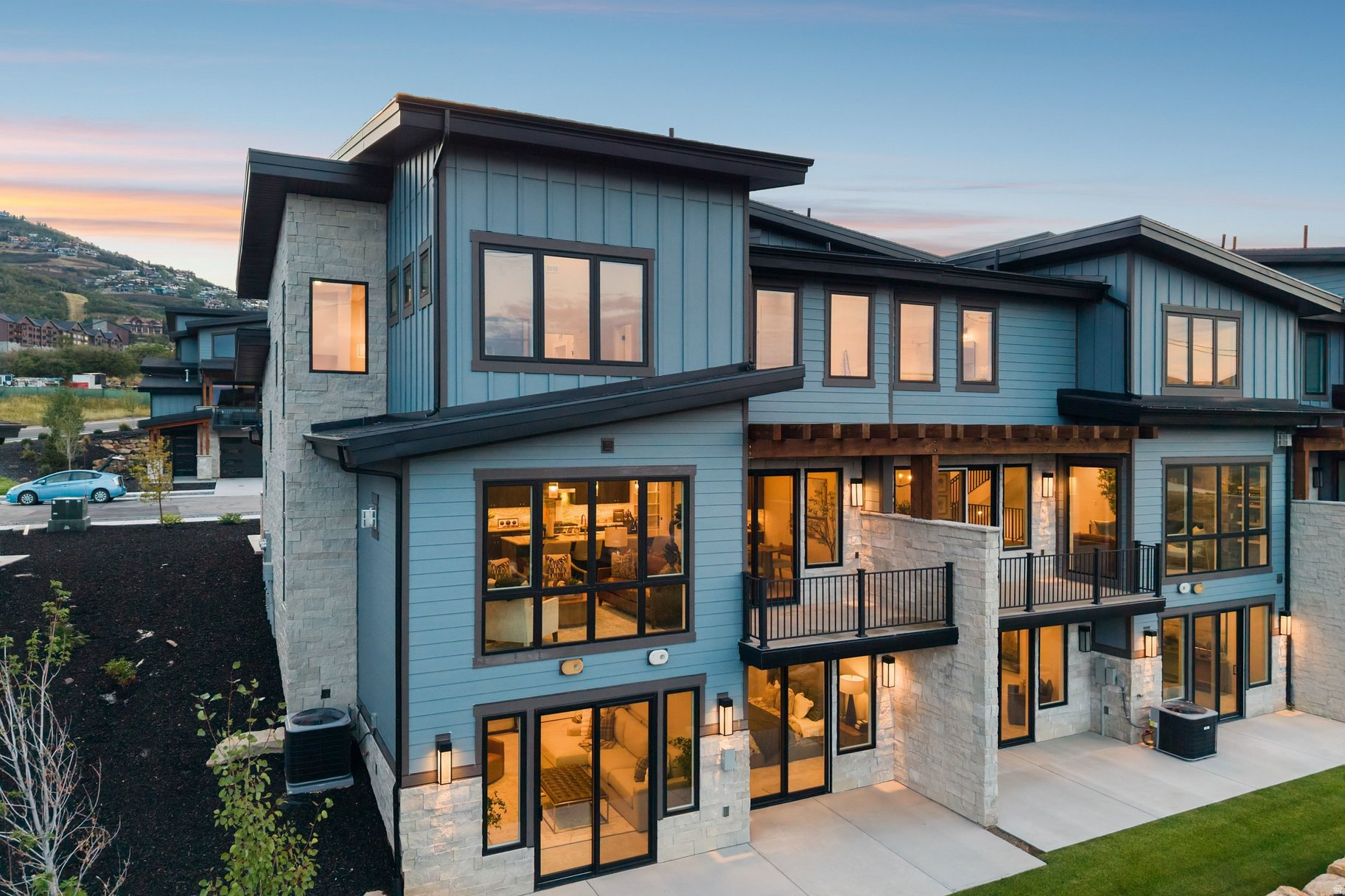 Modern blue-gray home with stone accents and illuminated windows at dusk.