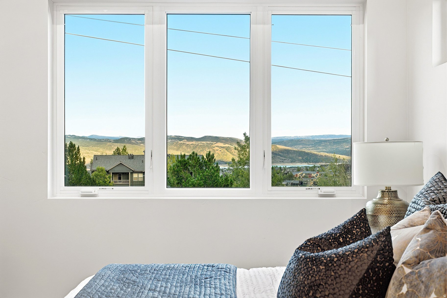 Bedroom with a wide window overlooking a lake and rolling mountain hills.